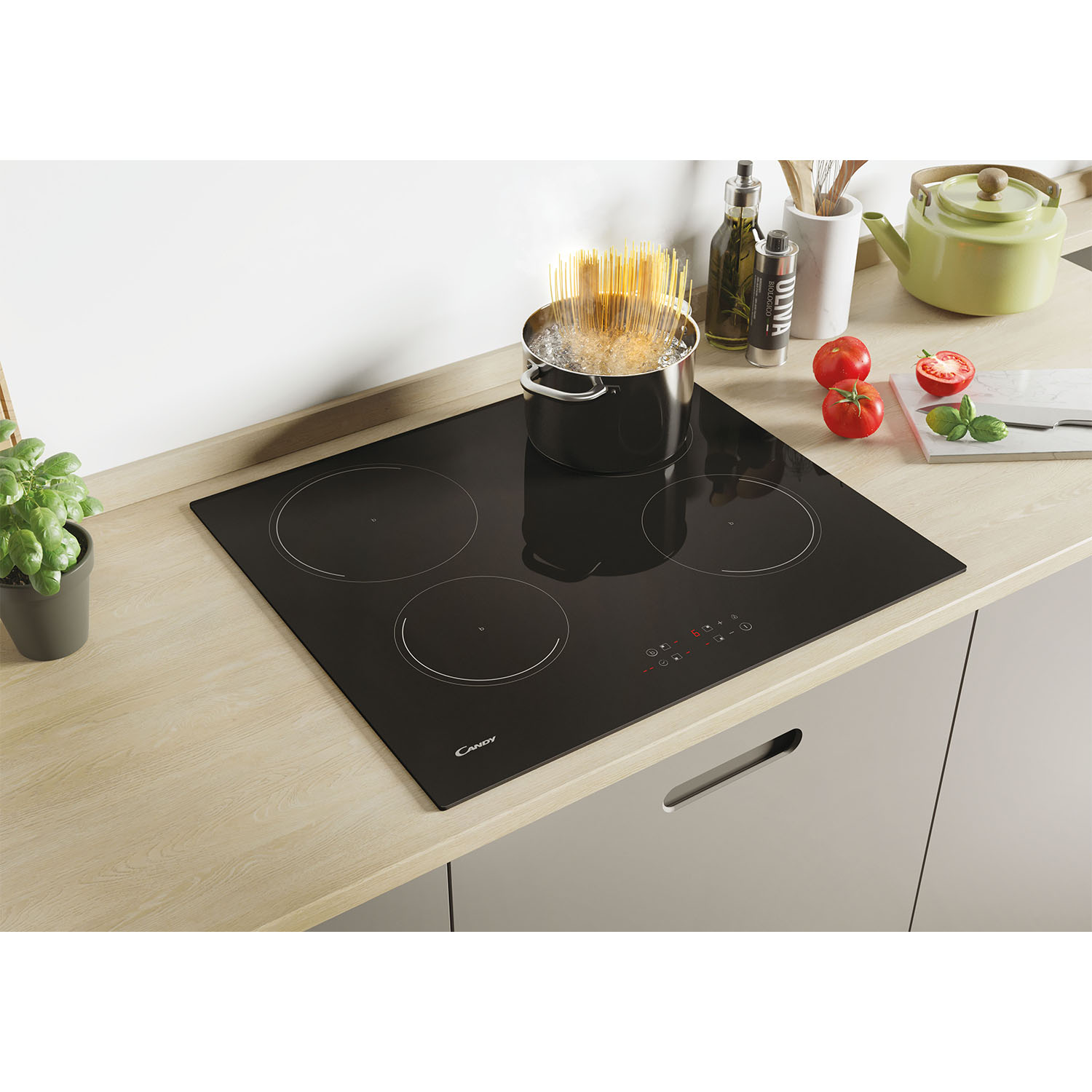 Piano cottura nero con pasta in cottura in pentola, pomodori e una teiera verde.