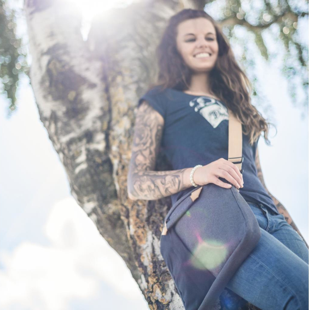 Een vrouw leunt tegen een boom, lachend, draagt een t-shirt en jeans.