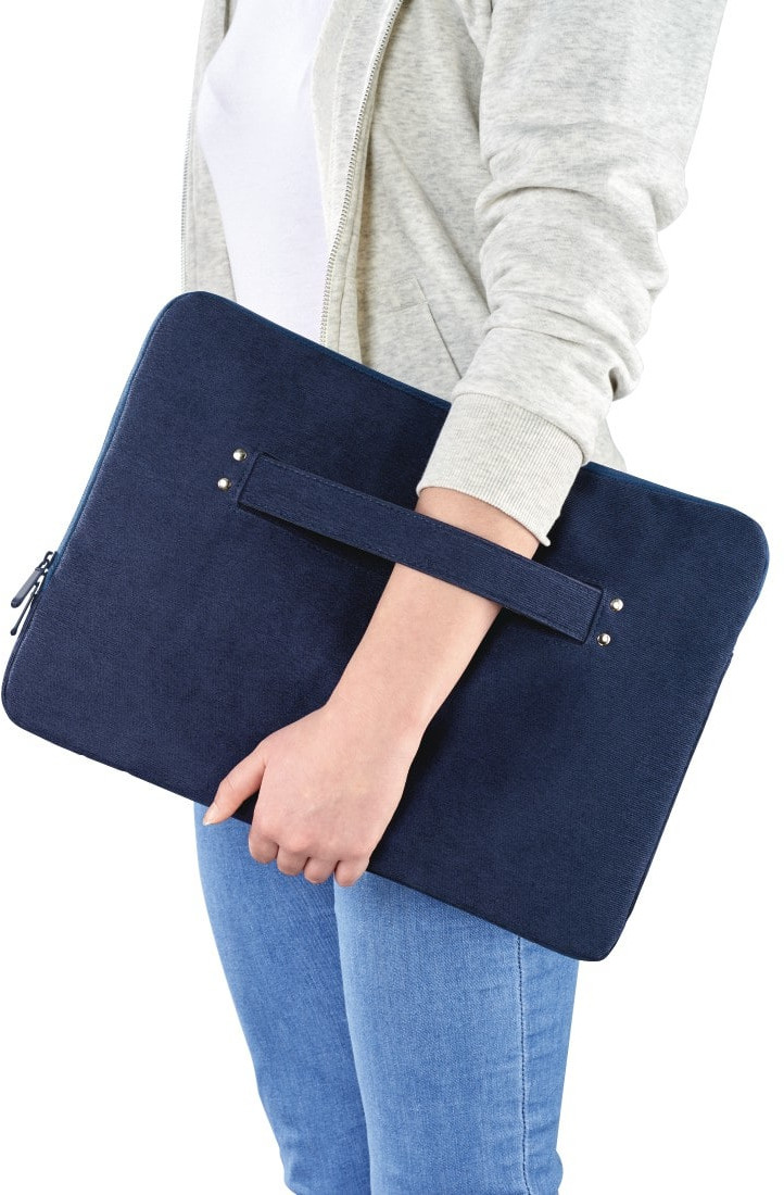 Personne tenant une housse bleue pour ordinateur portable avec une poignée, portant un jean et une veste grise.