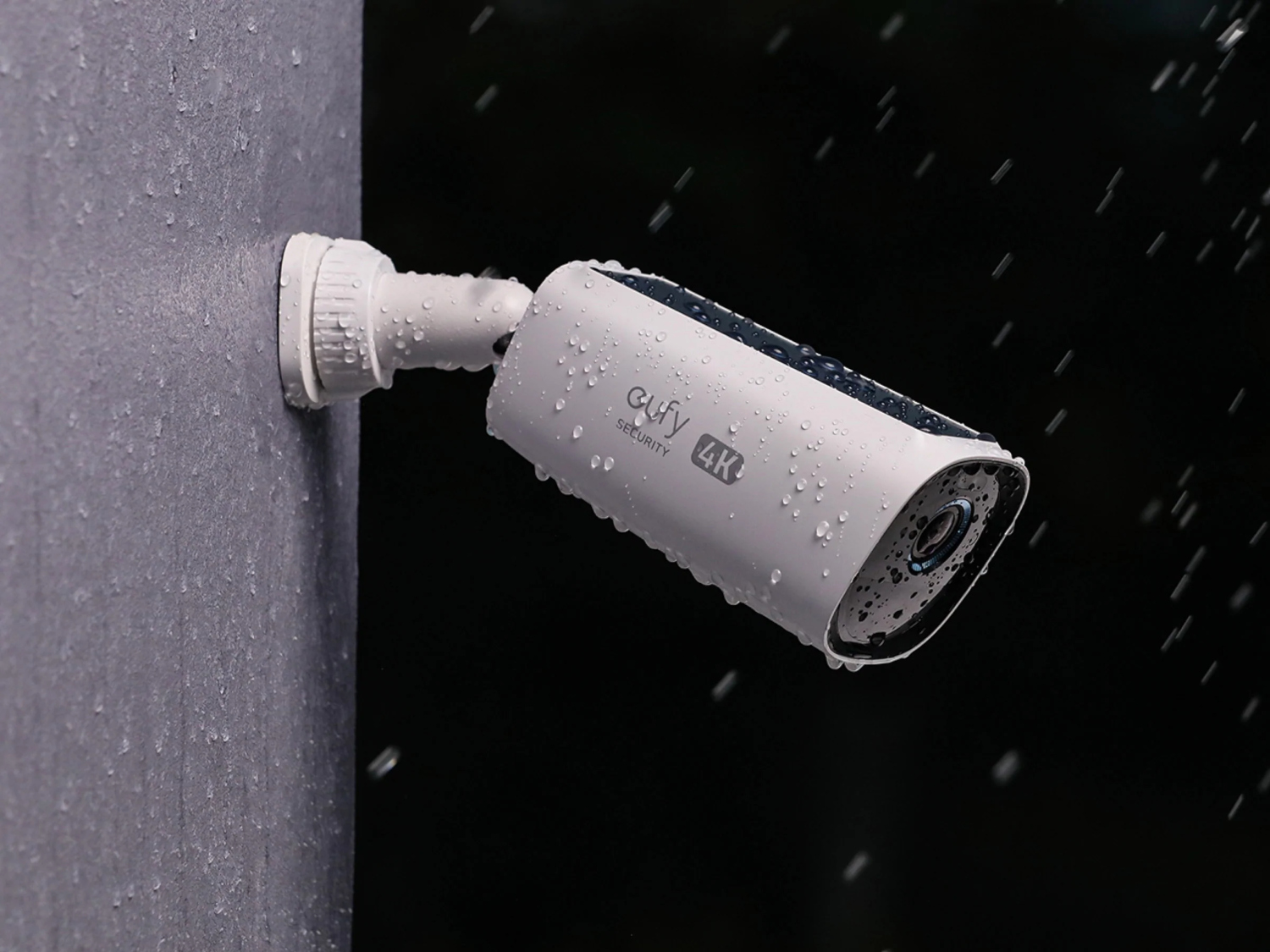 Une caméra de sécurité blanche est fixée sur un mur. Il pleut, et des gouttelettes d'eau recouvrent la caméra et le mur. Fond noir.