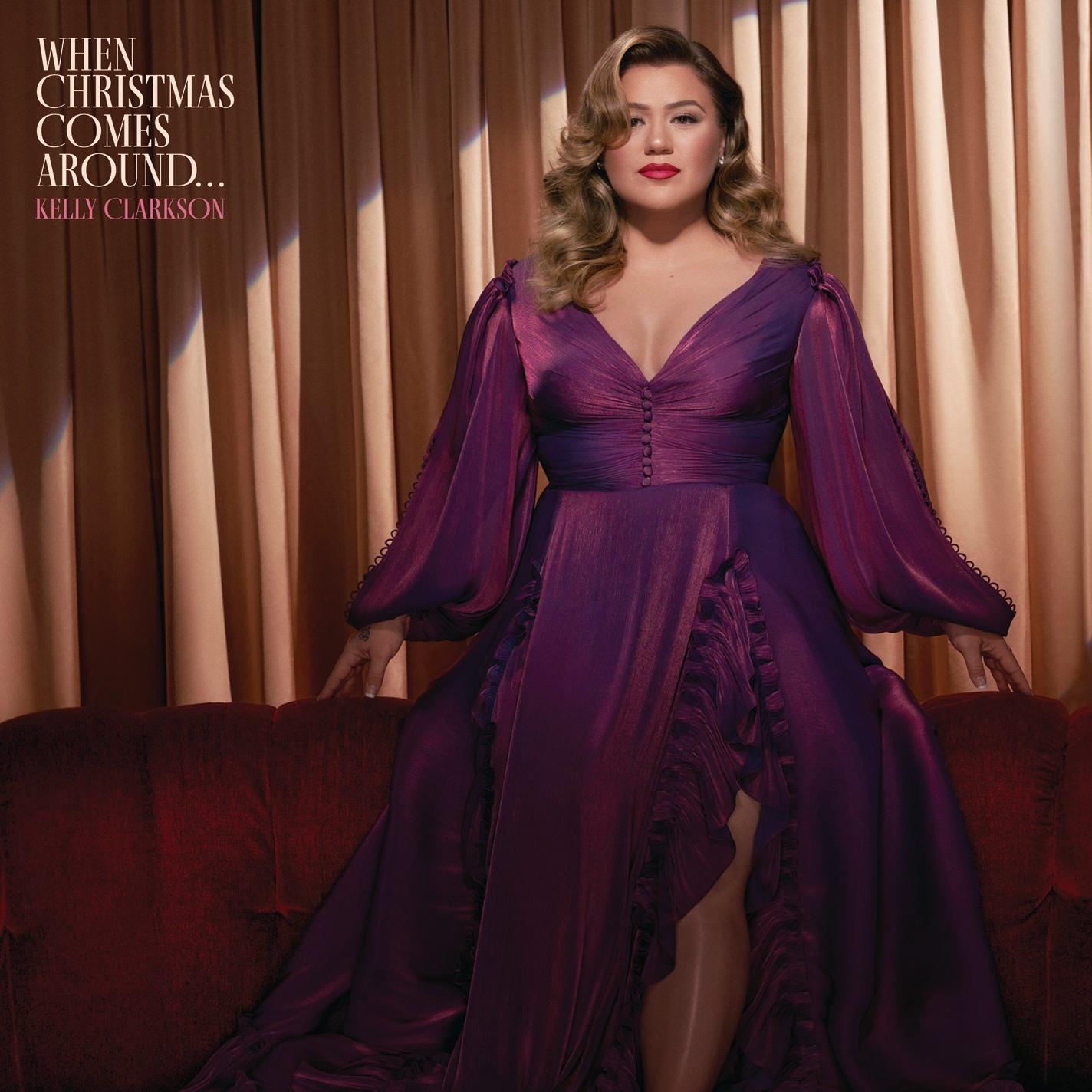 Kelly Clarkson Albumcover. Sie trägt ein lila Kleid und sitzt auf Sofa.