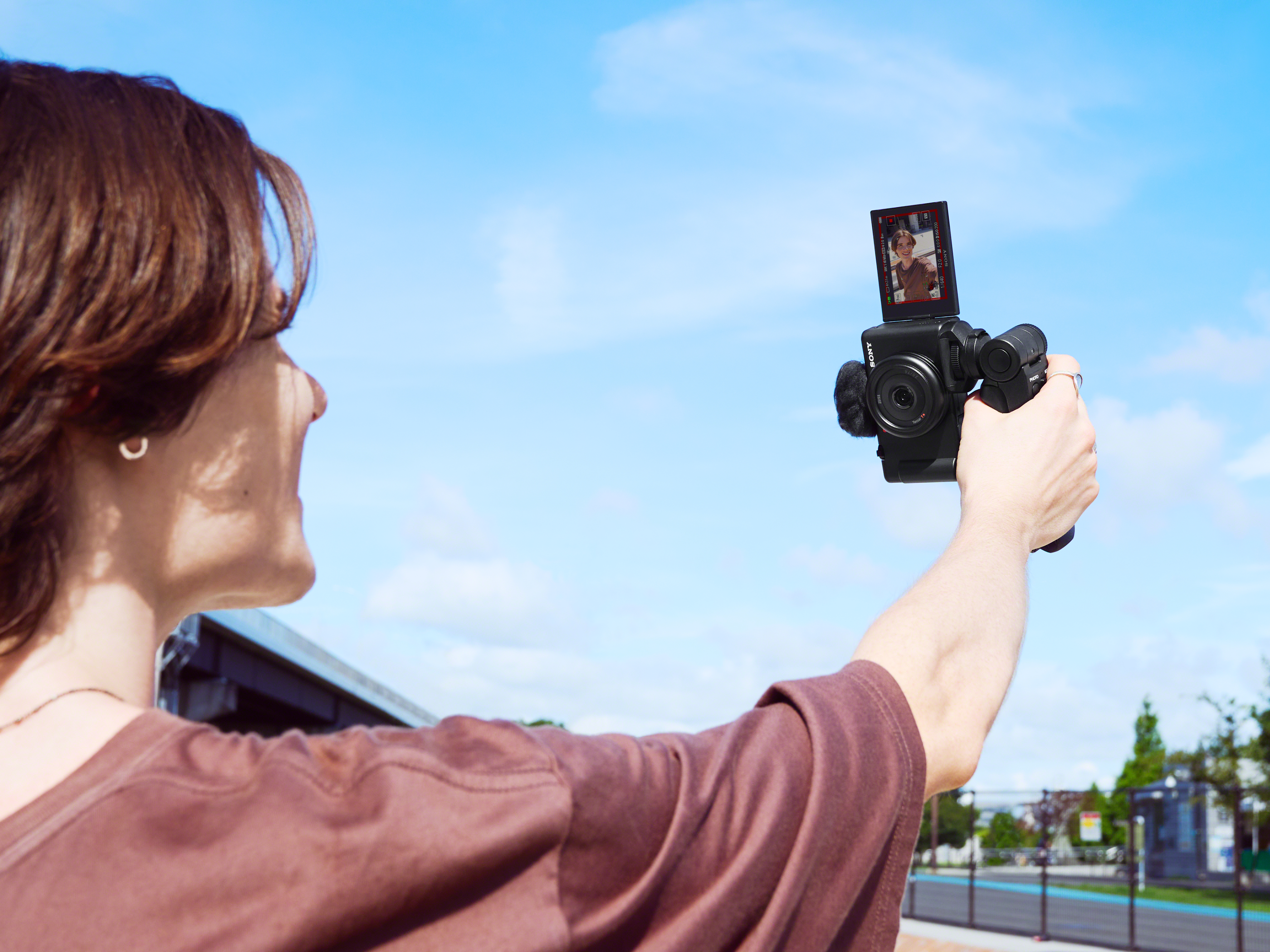 Una persona che tiene una fotocamera, registrando di fronte a un cielo blu.