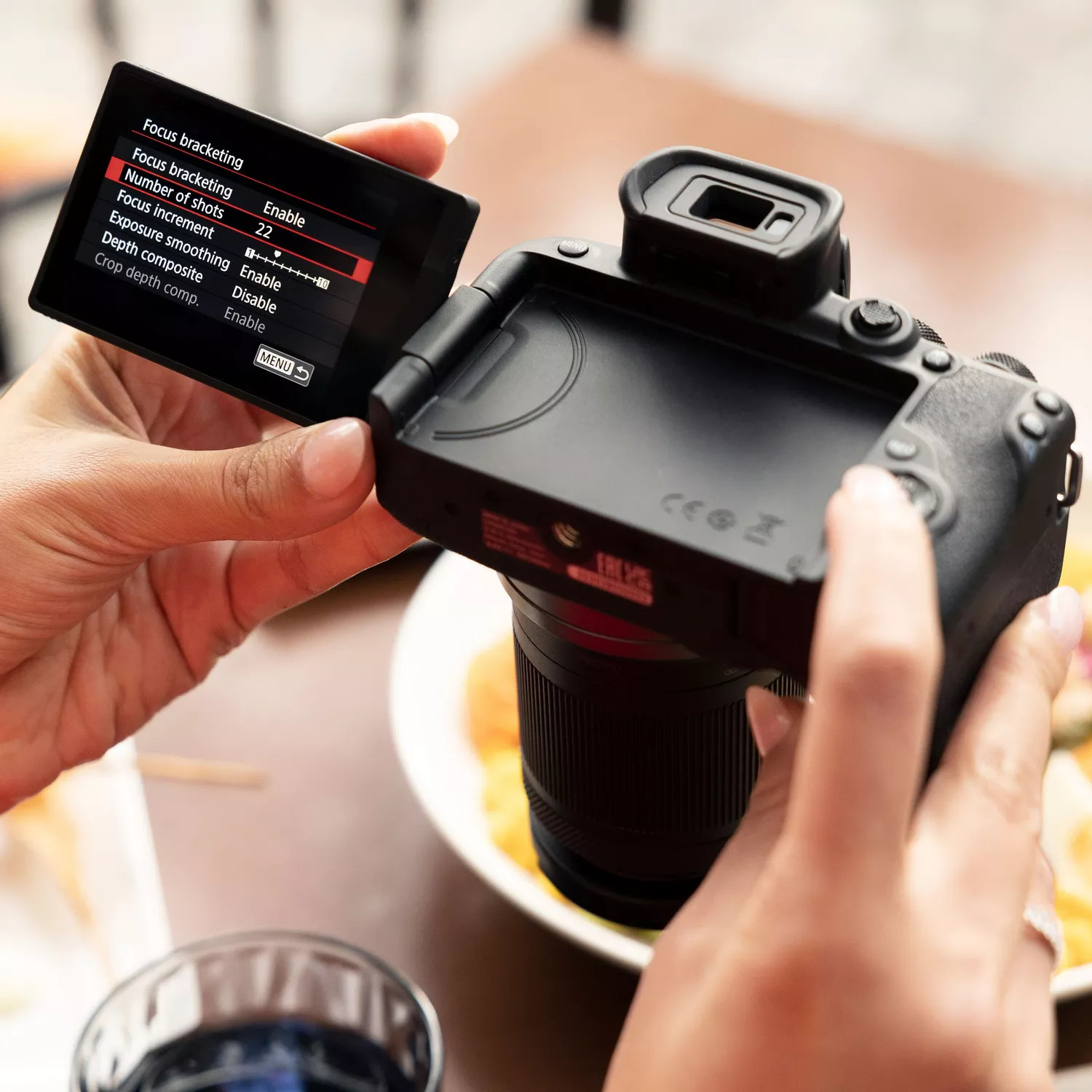 Woman holding a camera. The screen shows focus bracketing settings.