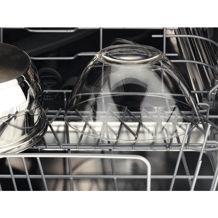 Un cuenco de vidrio transparente en una rejilla de lavavajillas, junto a una olla de acero inoxidable.
