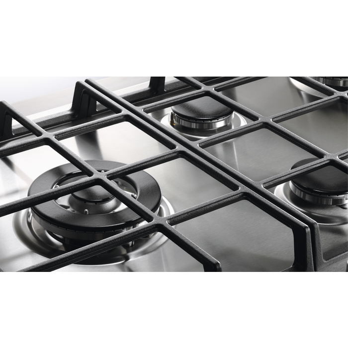 Primer plano de una encimera de gas con rejillas negras y quemadores plateados. Superficie de acero inoxidable.