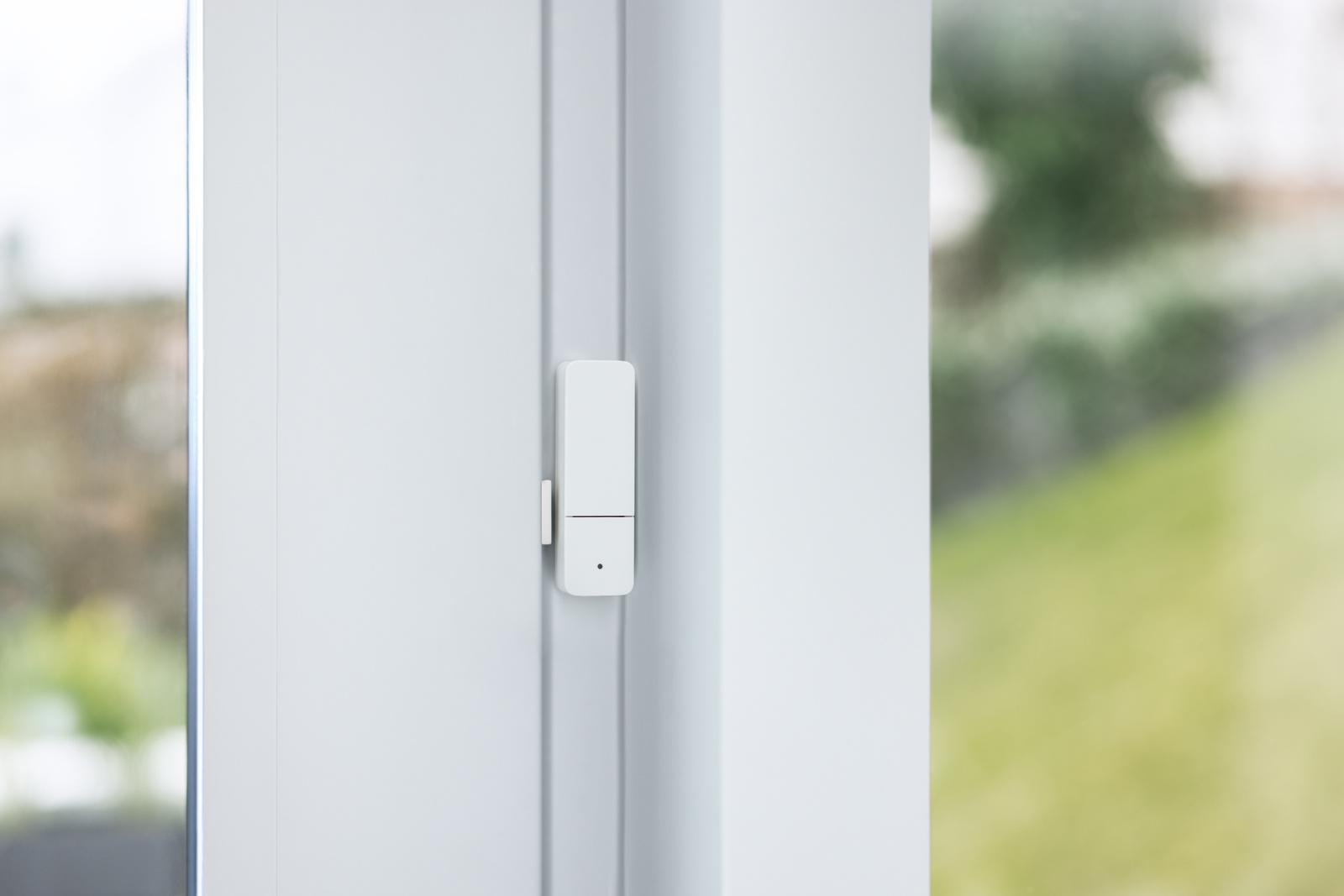 Ein kleines weißes Gerät an einem weißen Fensterrahmen befestigt, möglicherweise ein Sensor.
