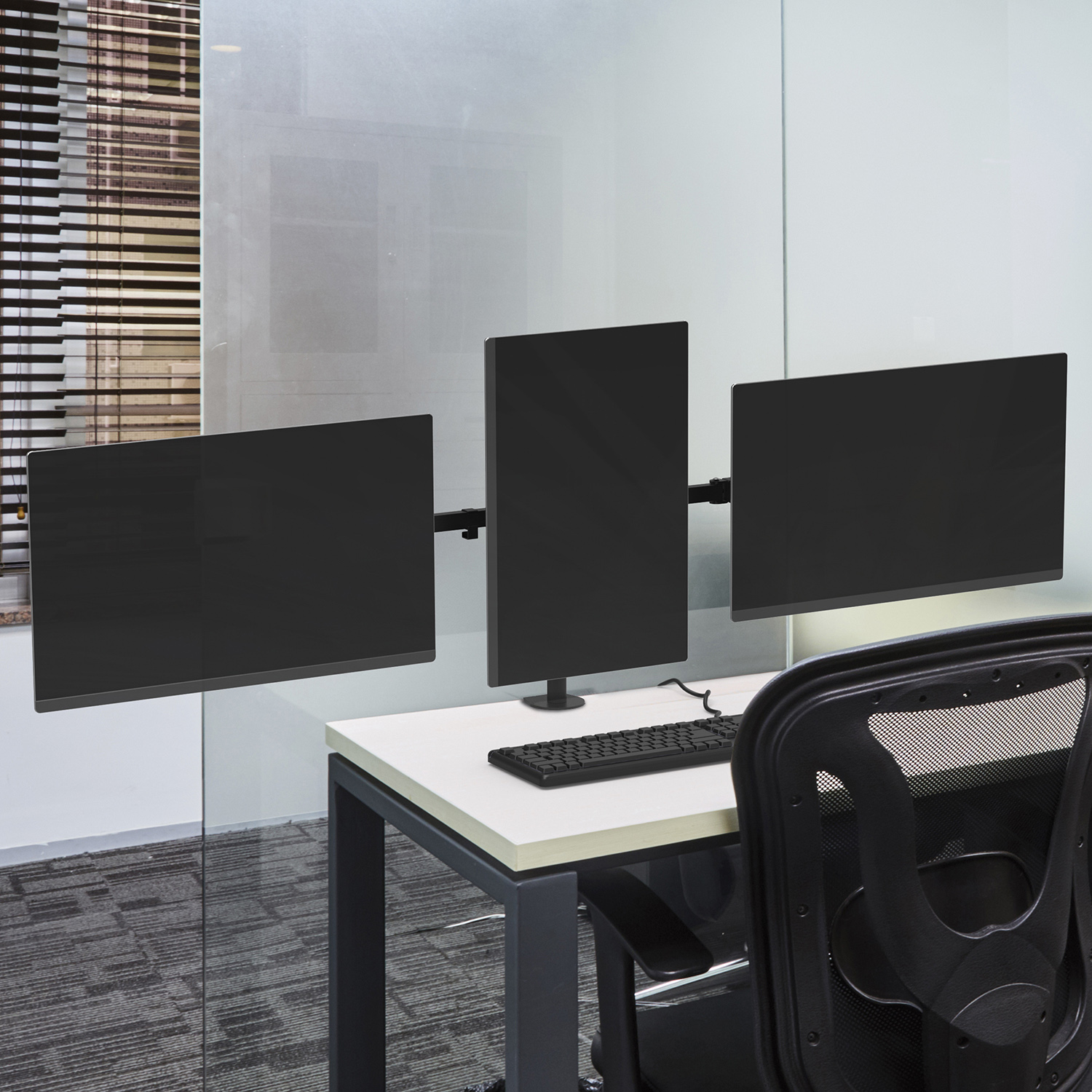 Three computer monitors mounted on a desk, with a keyboard and mouse, in an office setting.