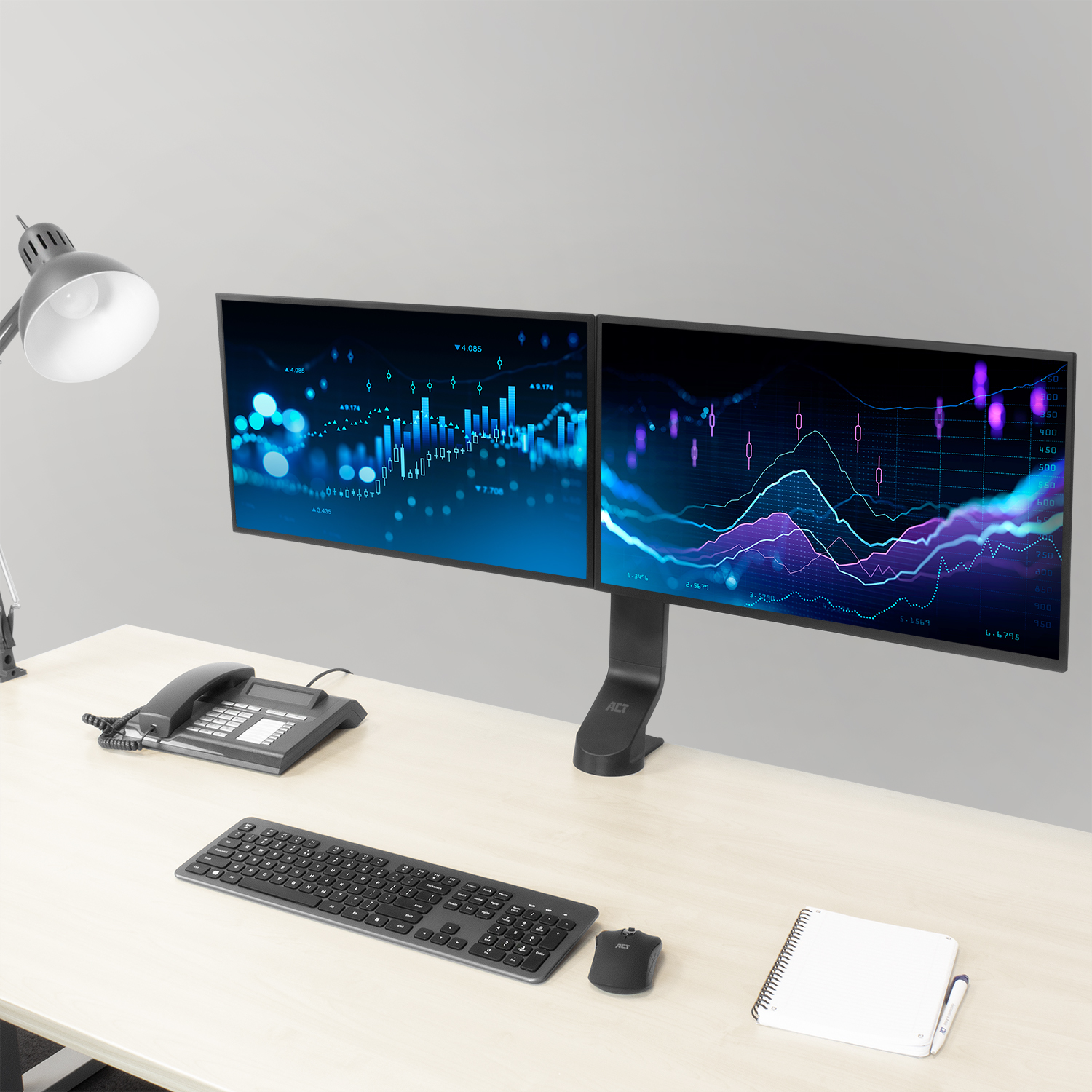 Two computer monitors displaying charts, on a desk with a lamp, keyboard, phone, and notebook.