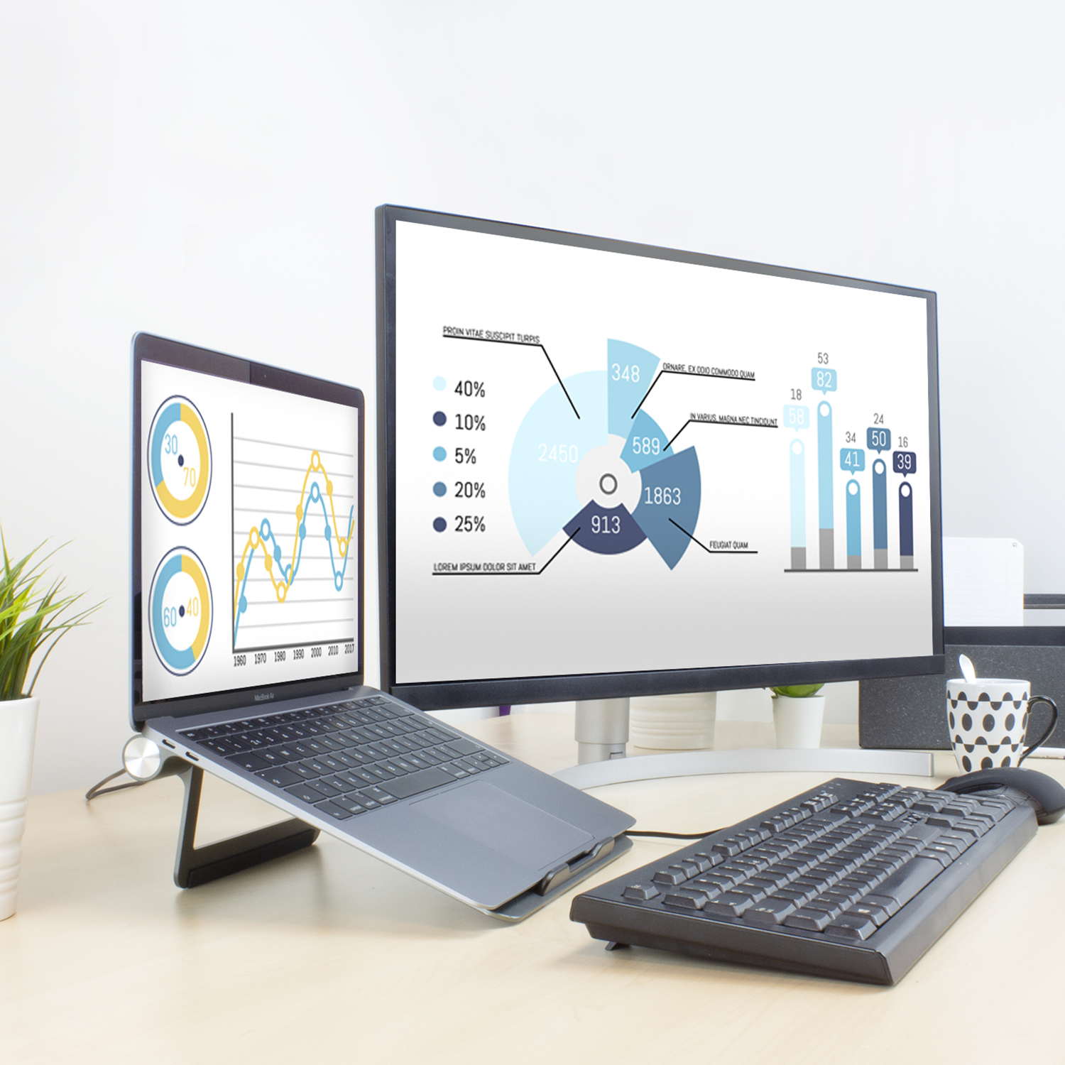 A laptop on a stand, a monitor, a keyboard, and a mouse on a desk with charts.