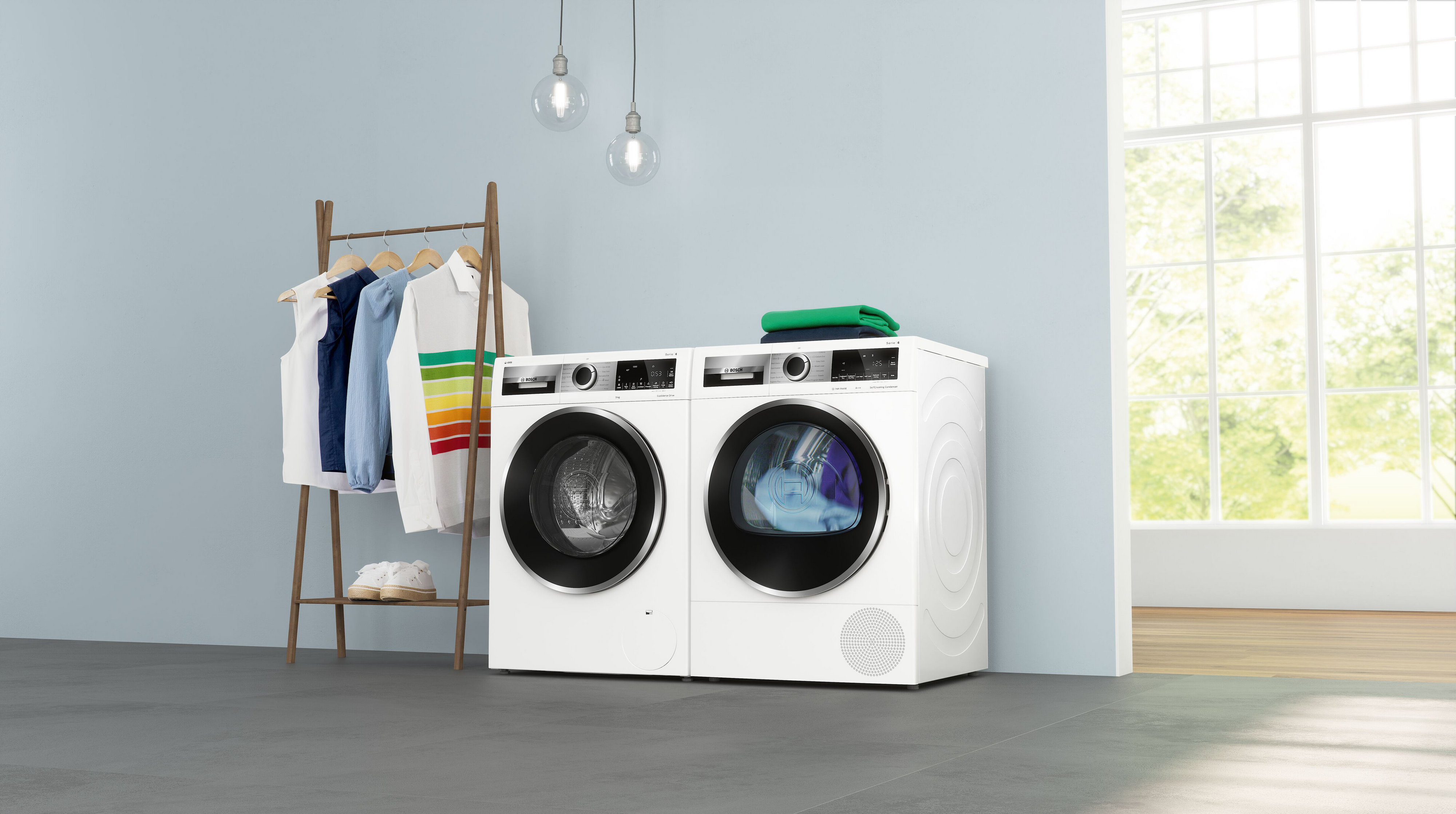 Twee witte wasmachines en een kledingrek met kleding in een lichtblauwe kamer.