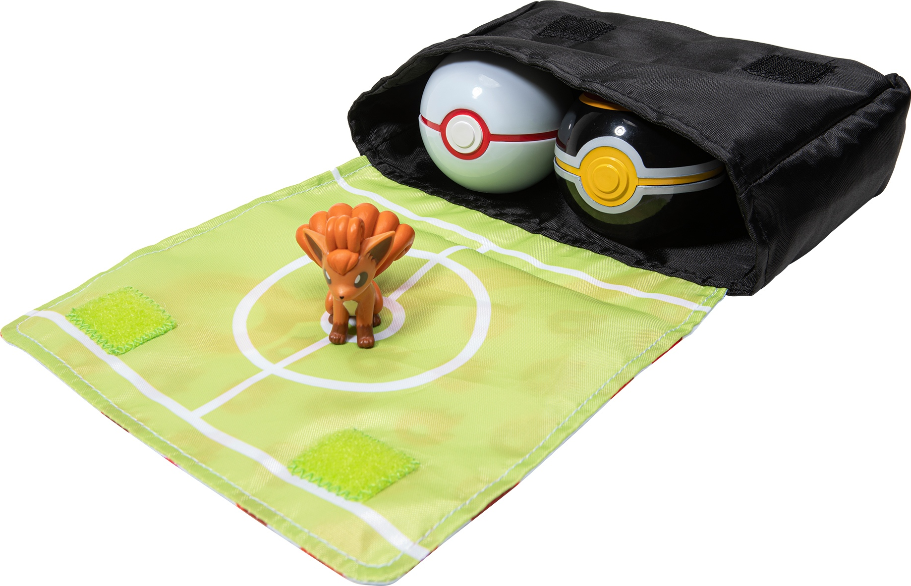 Une pochette noire contenant deux Poké Balls, avec un jouet Vulpix sur un tapis de jeu vert.