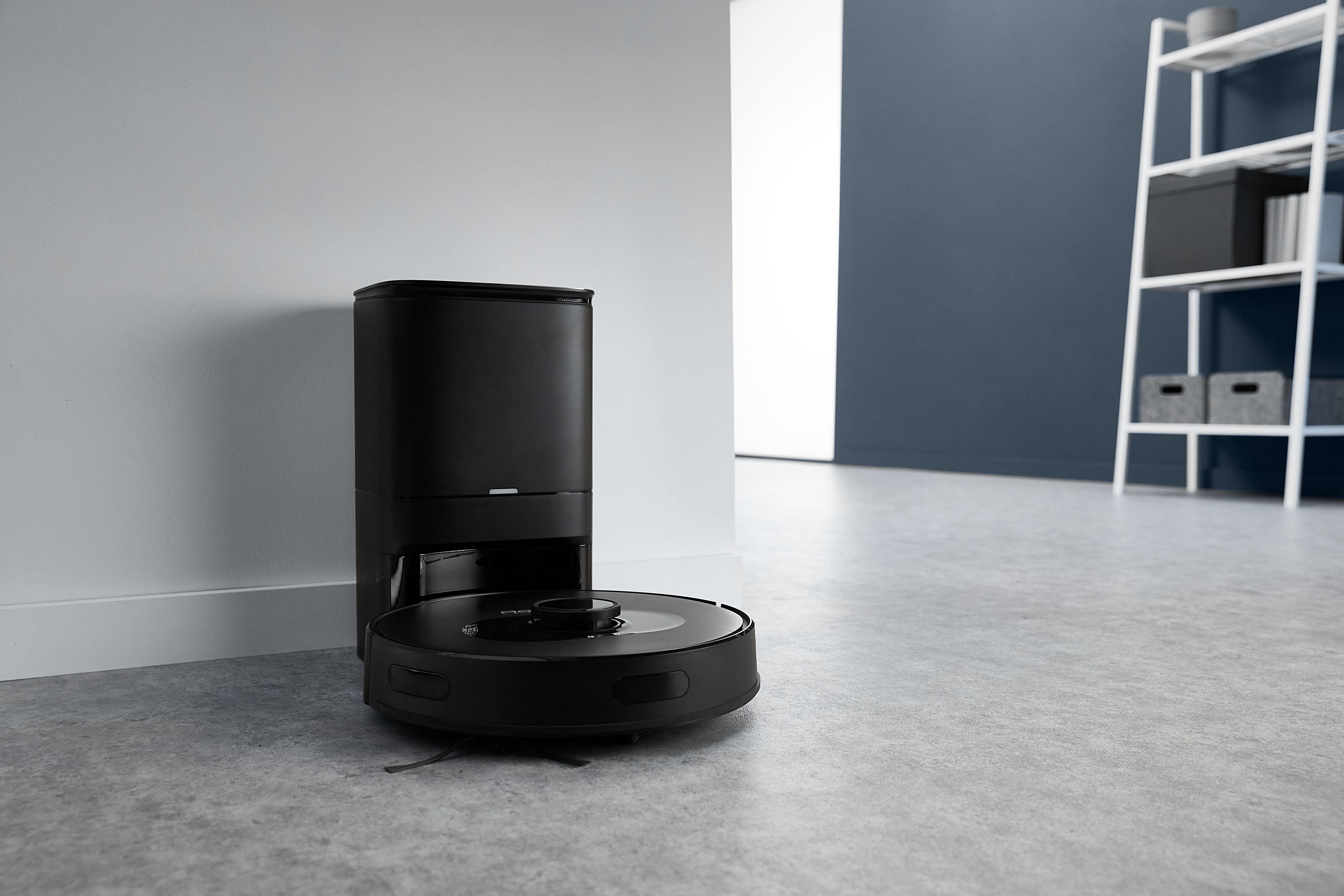 Ein schwarzer Roboter-Staubsauger neben einer schwarzen Ladestation in einem Raum.