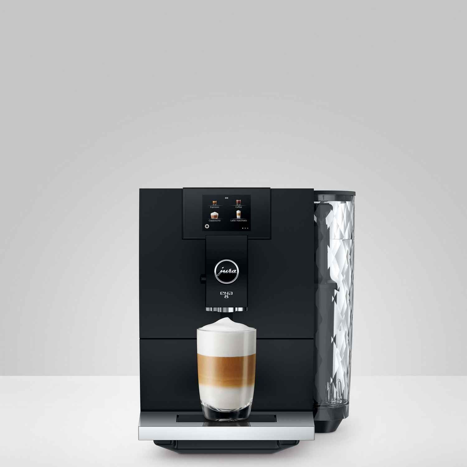 Black coffee machine with a glass of latte macchiato on a white surface.