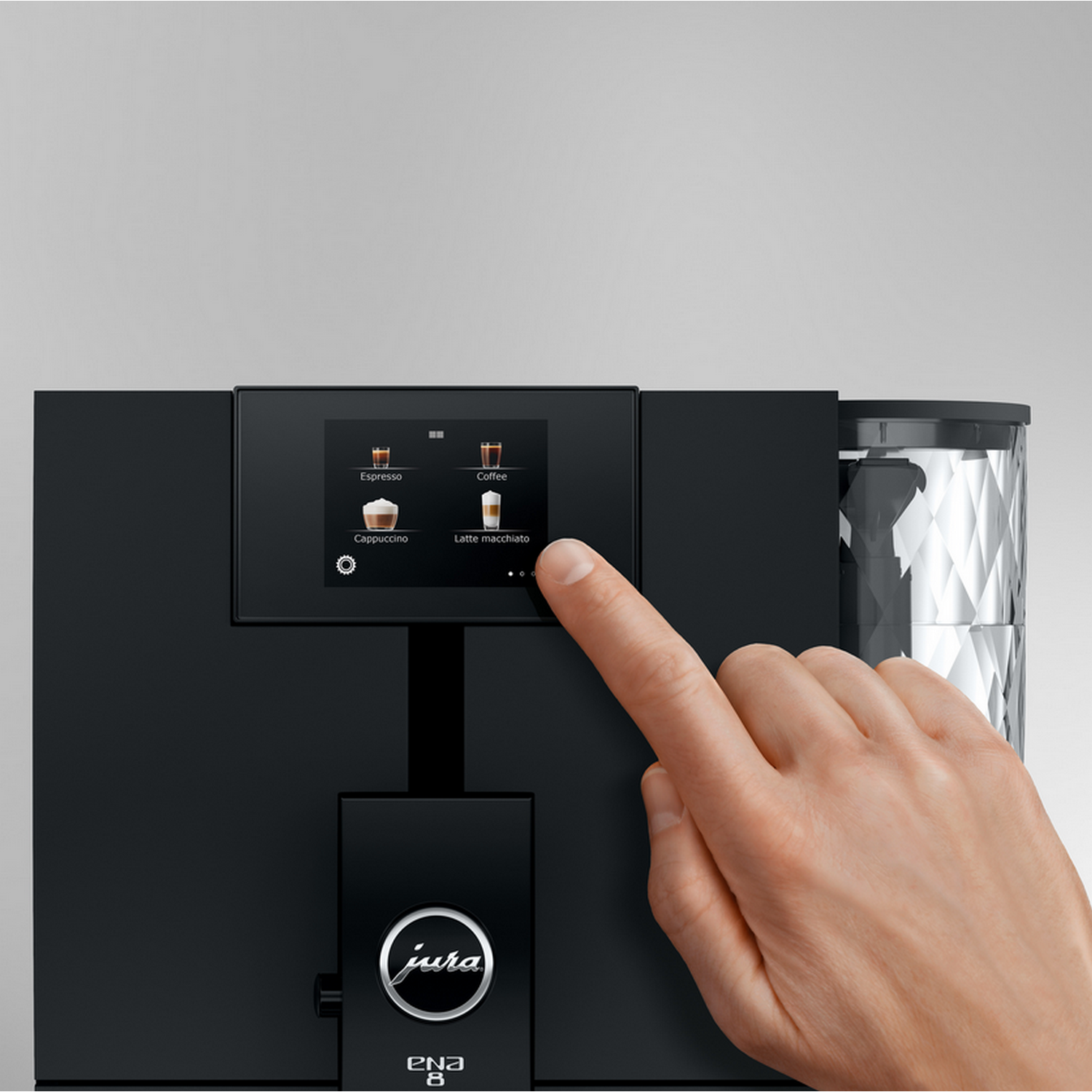 A hand touches a coffee machine screen, selecting 'Latte macchiato'. Machine is black, has 'jura' logo. Background is light grey.