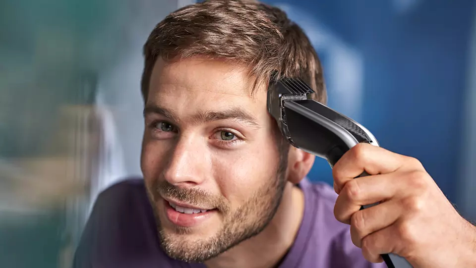 Ein Mann mit braunen Haaren schneidet sich mit einem schwarzen Haarschneider die Haare.