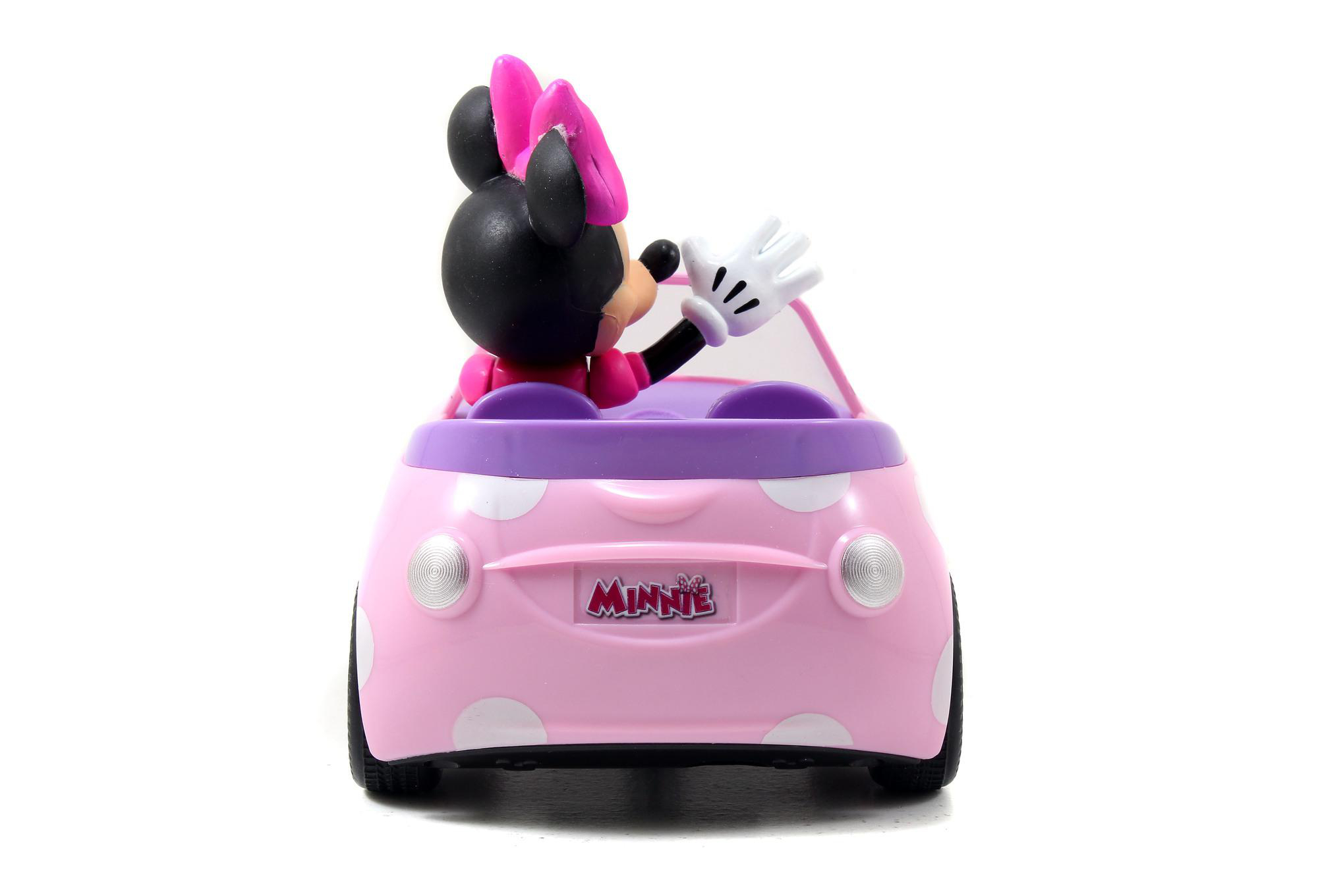 Minnie Mouse in einem rosa Polka-Dot-Auto, winkt vom Fahrersitz, weißer Hintergrund.