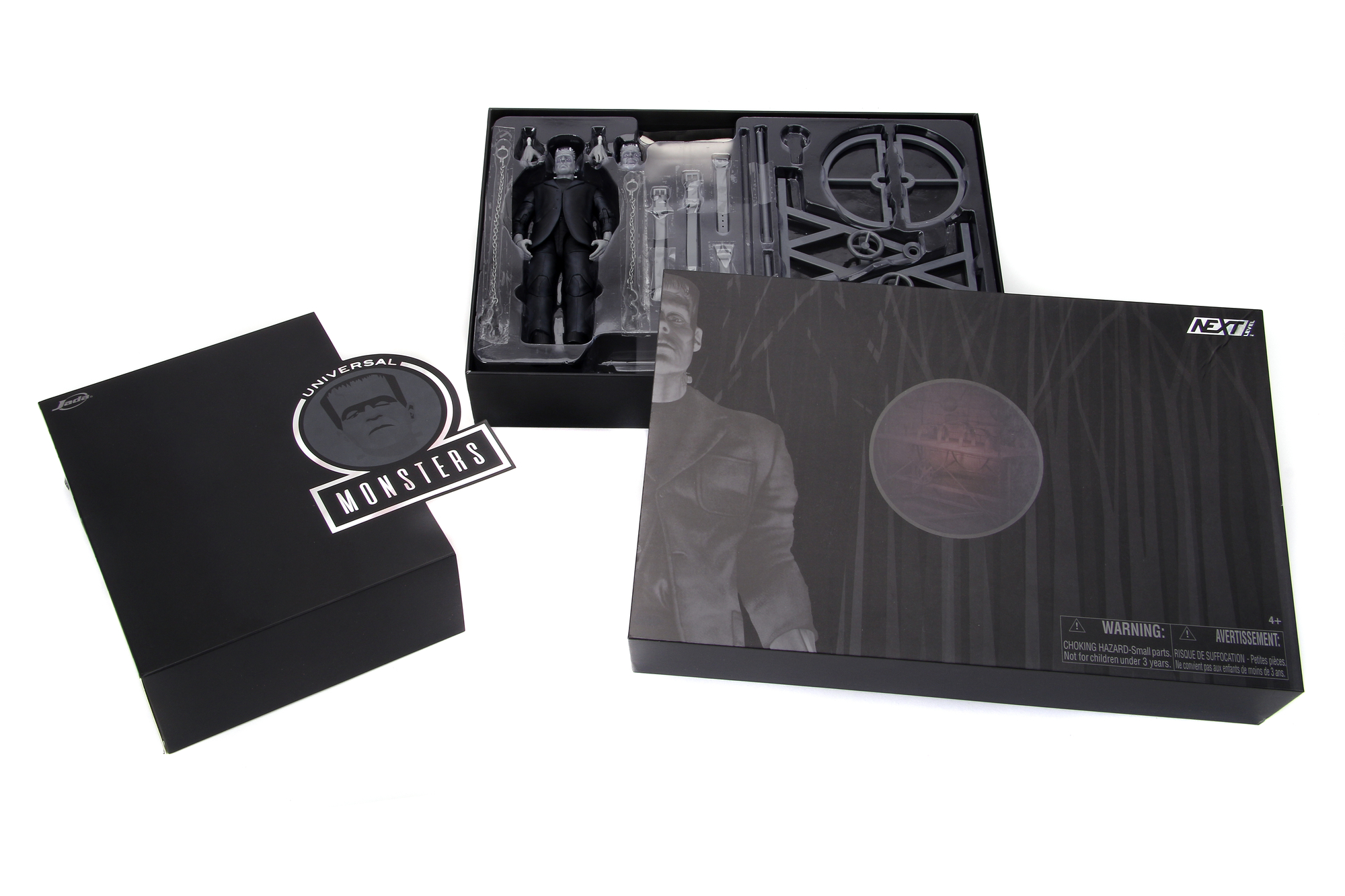 Schwarze Boxen mit einer Frankenstein-Figur, eine Box mit Aufkleber und eine dunkle Illustration auf weißer Oberfläche.
