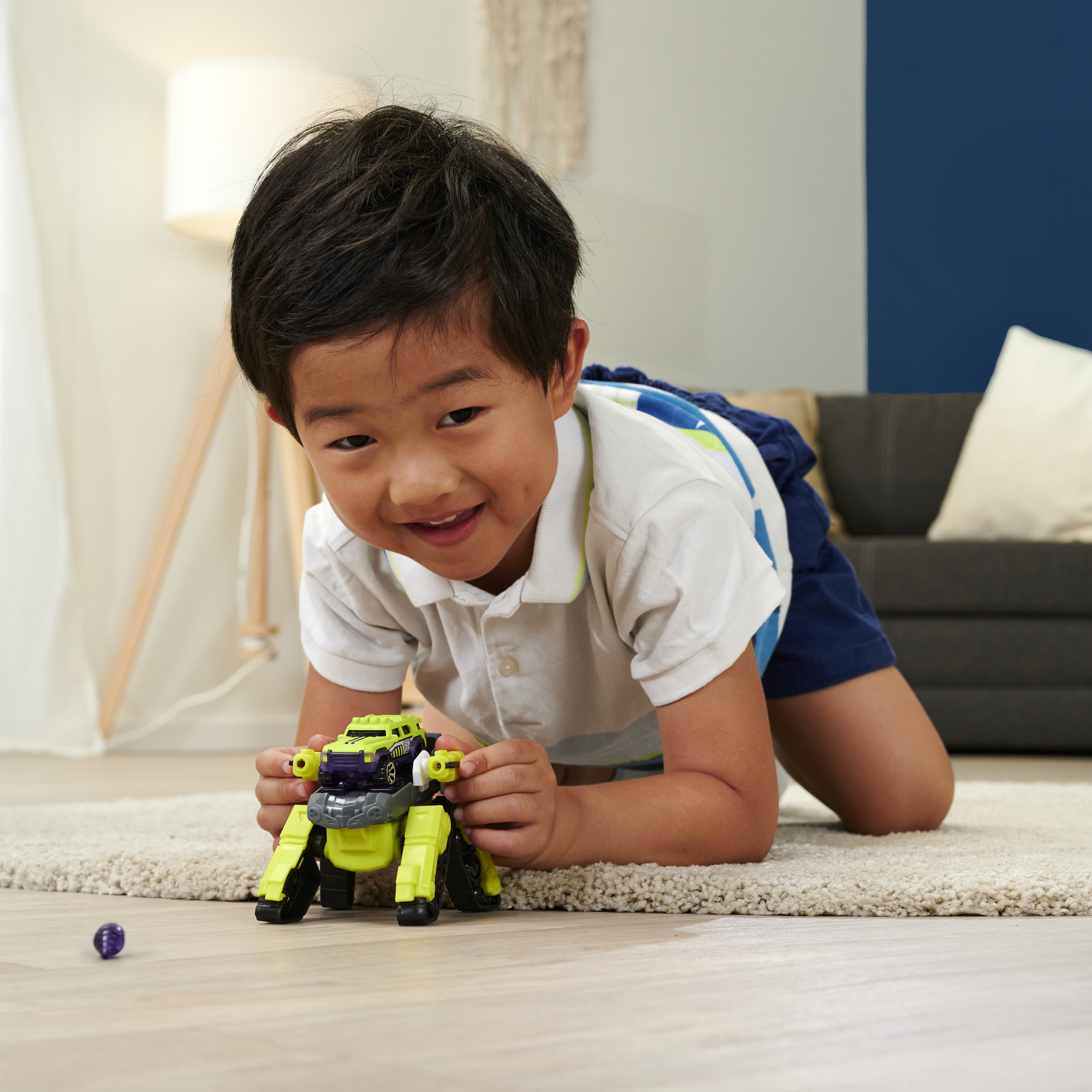 Ein Kind spielt mit einem gelb-lila Transformer-Spielzeugauto. Das Kind lächelt.