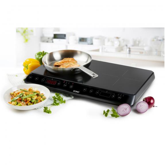 Inductiekookplaat met pan, eten, groenten en verse ingrediënten.
