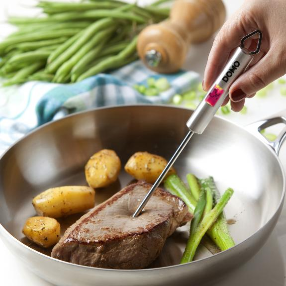 A steak is being measured for doneness with a thermometer in a pan with potatoes.