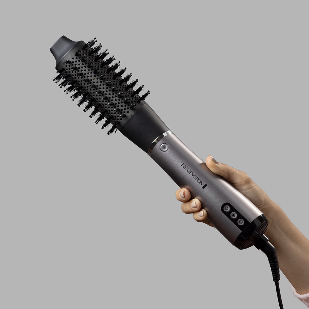 Kéz egy szürke Remington hajformázó kefét tart fekete sörtékkel.