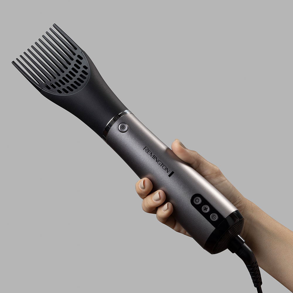 Egy kéz egy szürke-fekete Remington hajszárítót tart, fésű tartozékkal.