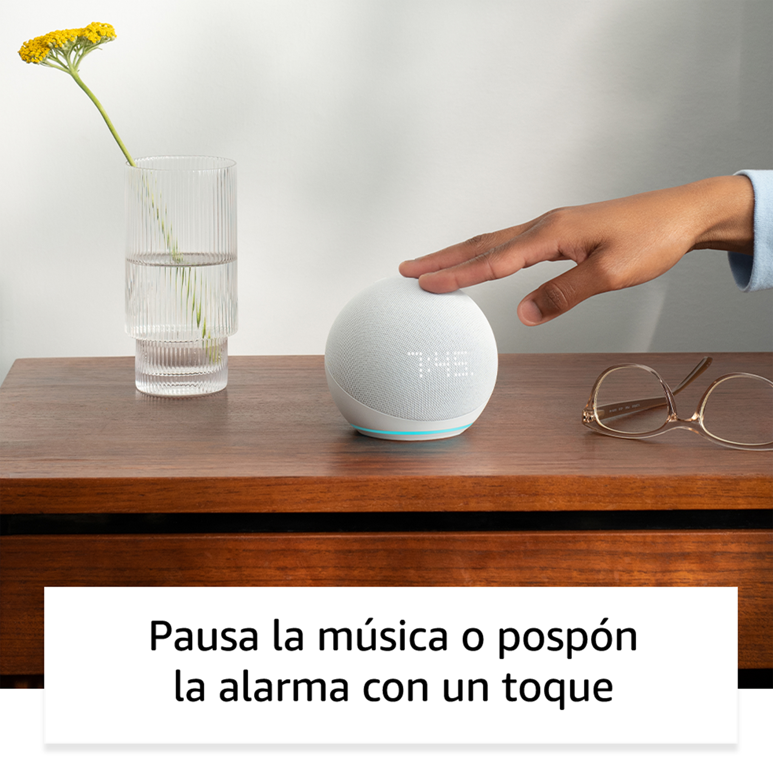 Un Echo Dot en una mesa de madera. Una mano lo toca.