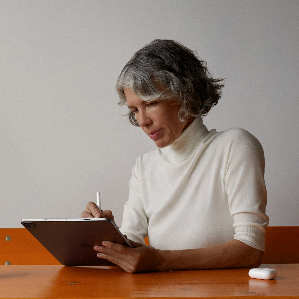 Mujer con pelo gris usando una tableta con un lápiz, mesa naranja.