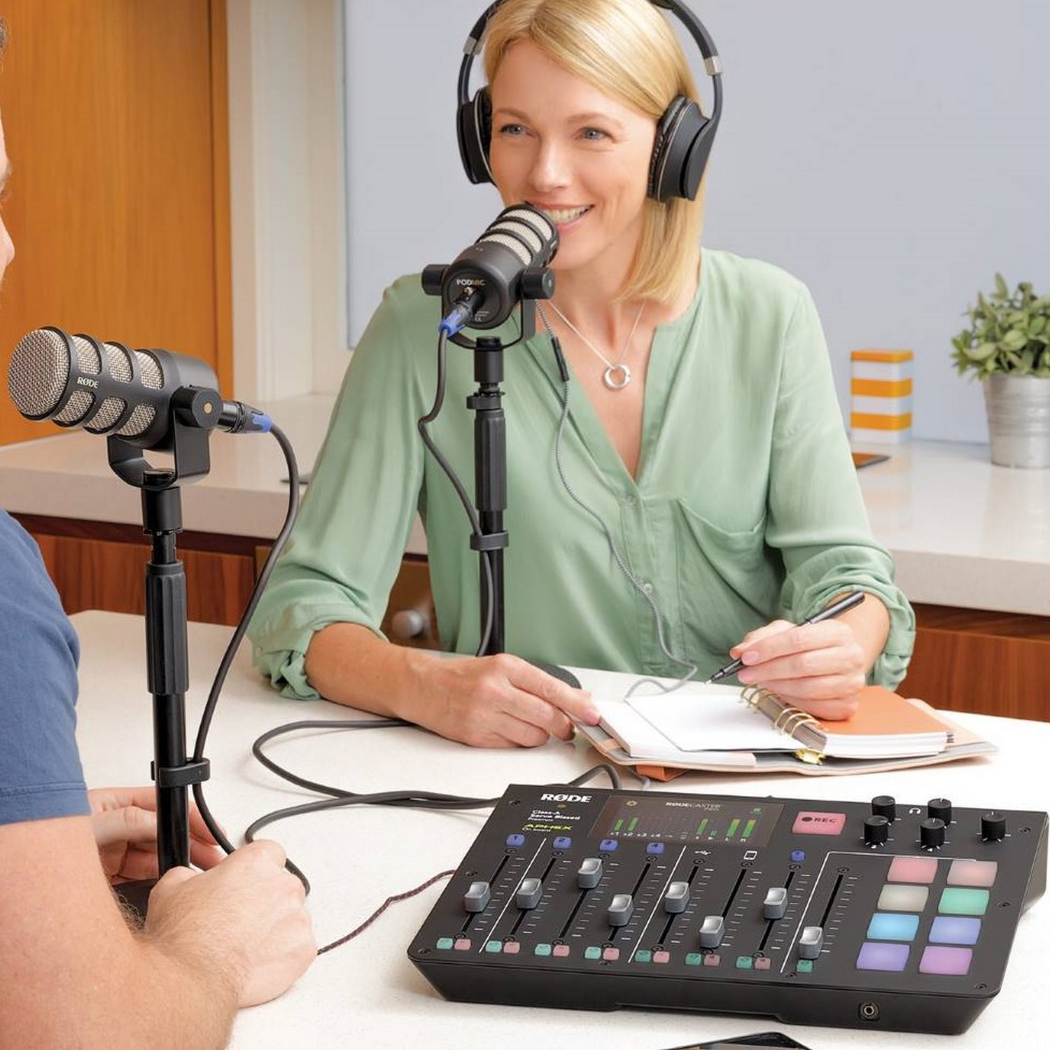 Two people recording a podcast with microphones and a soundboard.