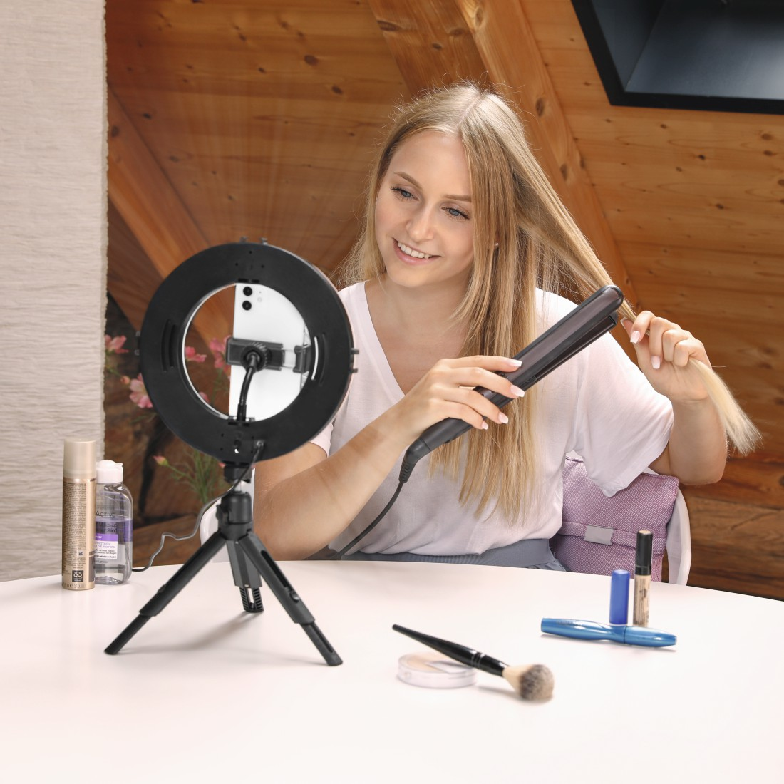 Blonde Frau benutzt einen Glätteisen mit Ringlicht und Make-up auf dem Tisch.