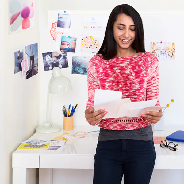 Une femme sourit en lisant des papiers sur un bureau avec des photos et une lampe.