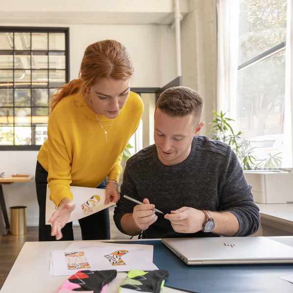 Deux personnes travaillent sur un design. L'une porte un pull jaune et l'autre un pull gris.