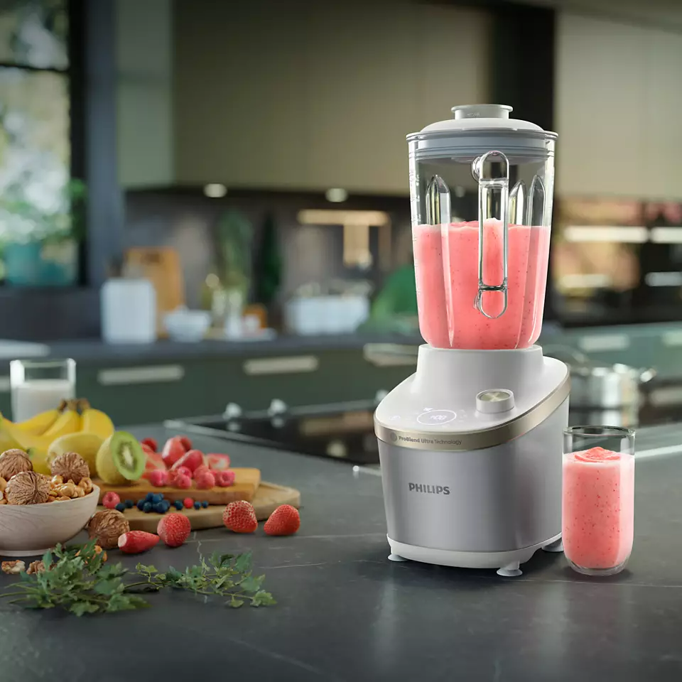 Turmixgép rózsaszín smoothie-val, gyümölcsökkel a táblán és egy pohár smoothie-val.
