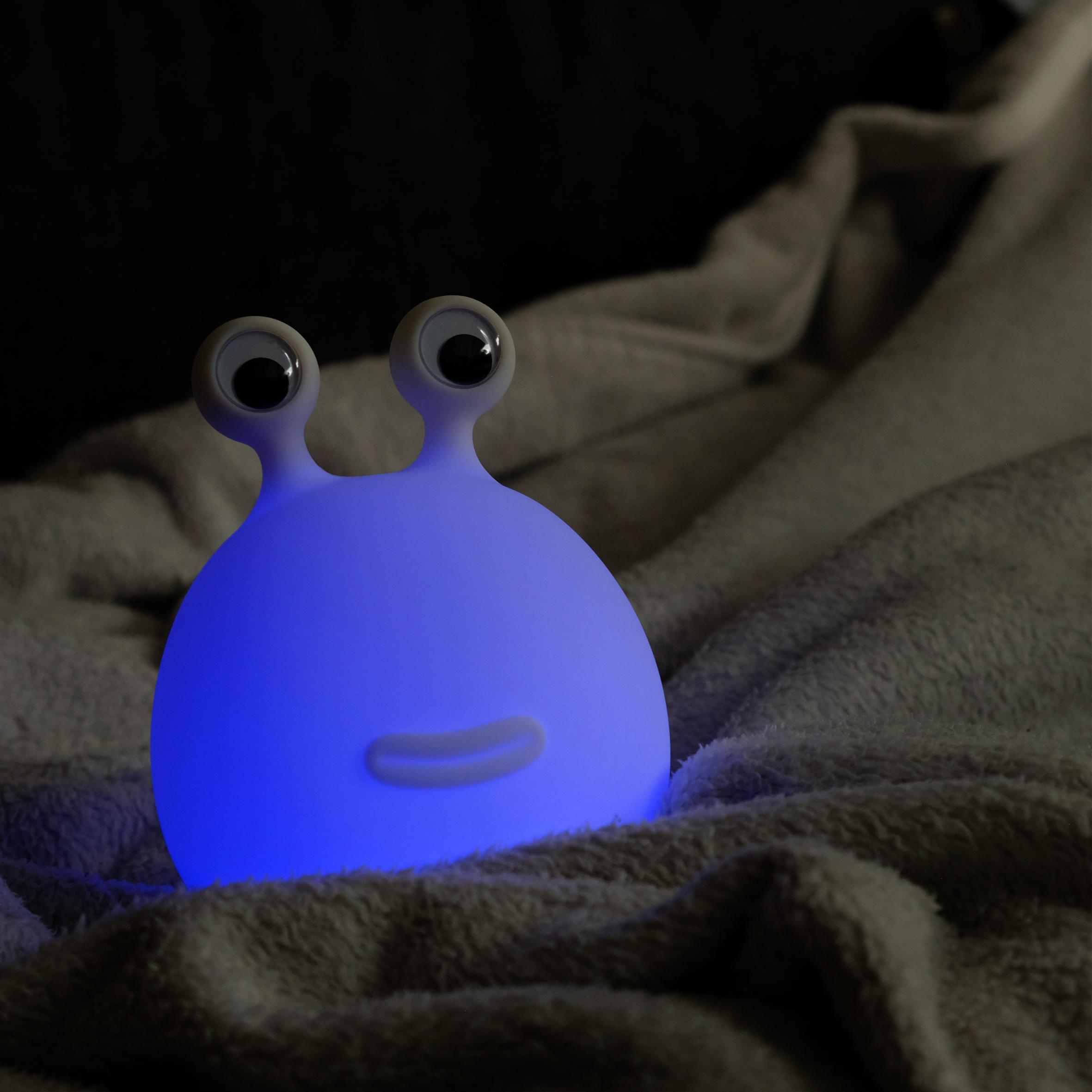 Ein blau leuchtendes Spielzeug-Alien auf einer weichen, grauen Decke in dunkler Umgebung.