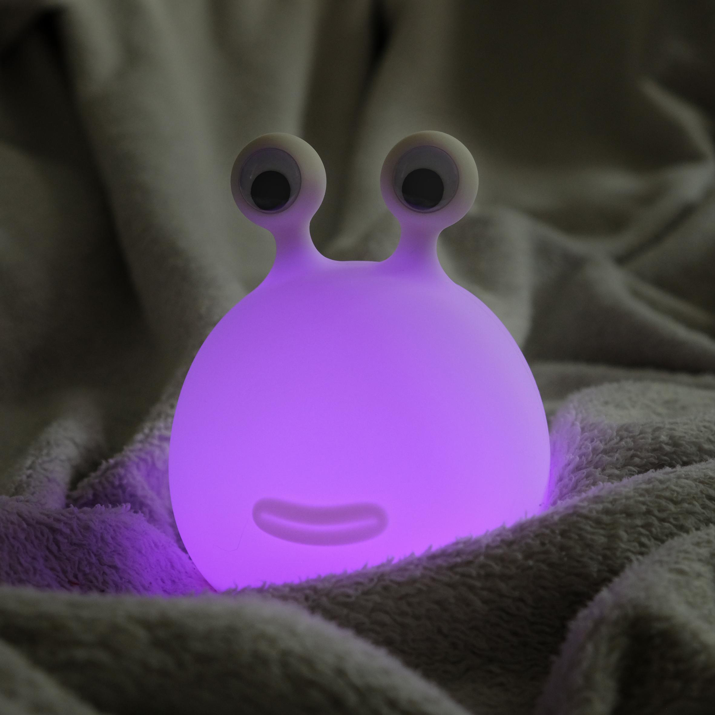 Lila leuchtende Alien-Lampe auf einer weichen, grauen Decke, weiße Augen.