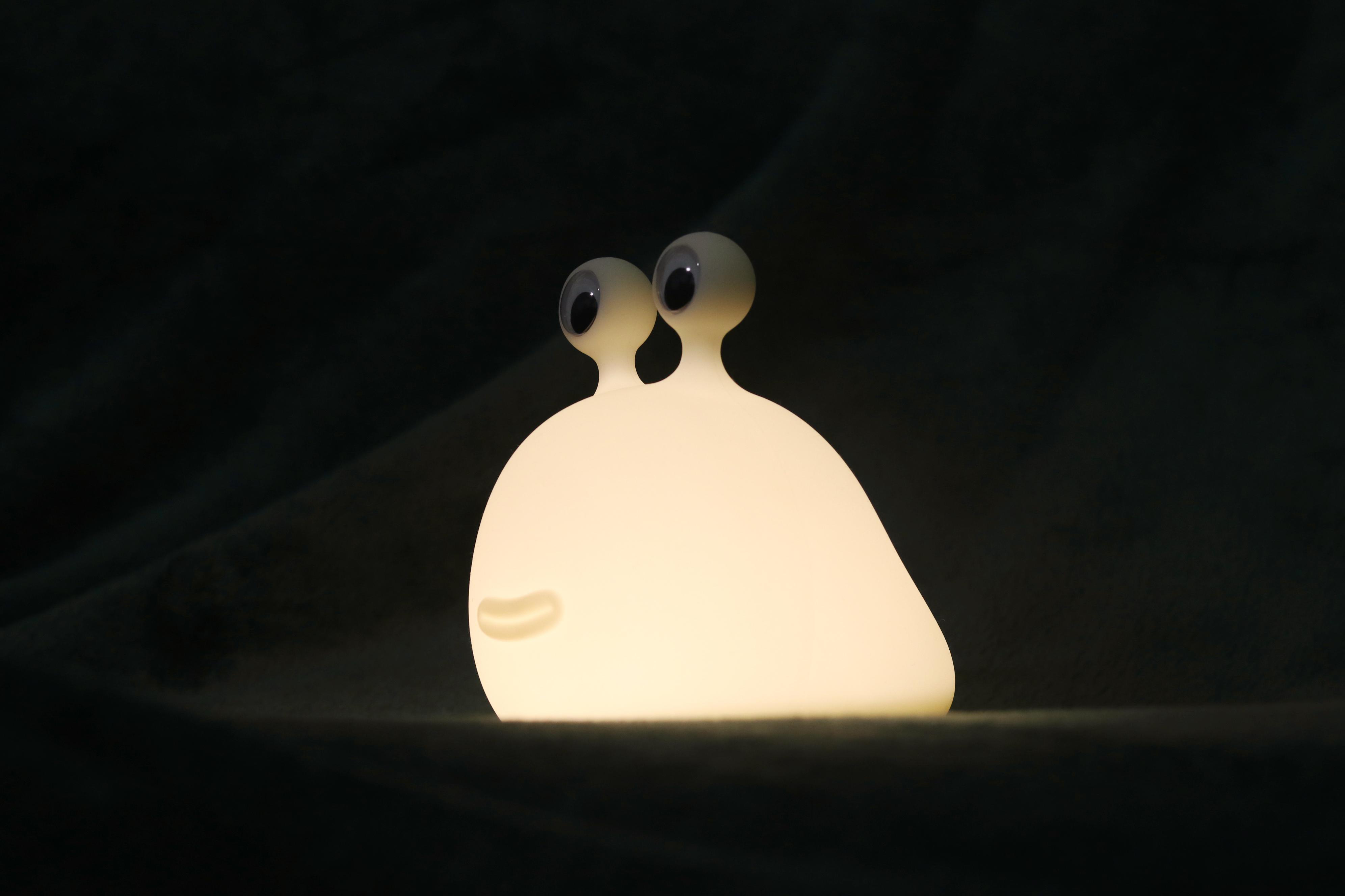 Eine weiße, schneckenförmige Lampe mit Wackelaugen im Dunkeln.