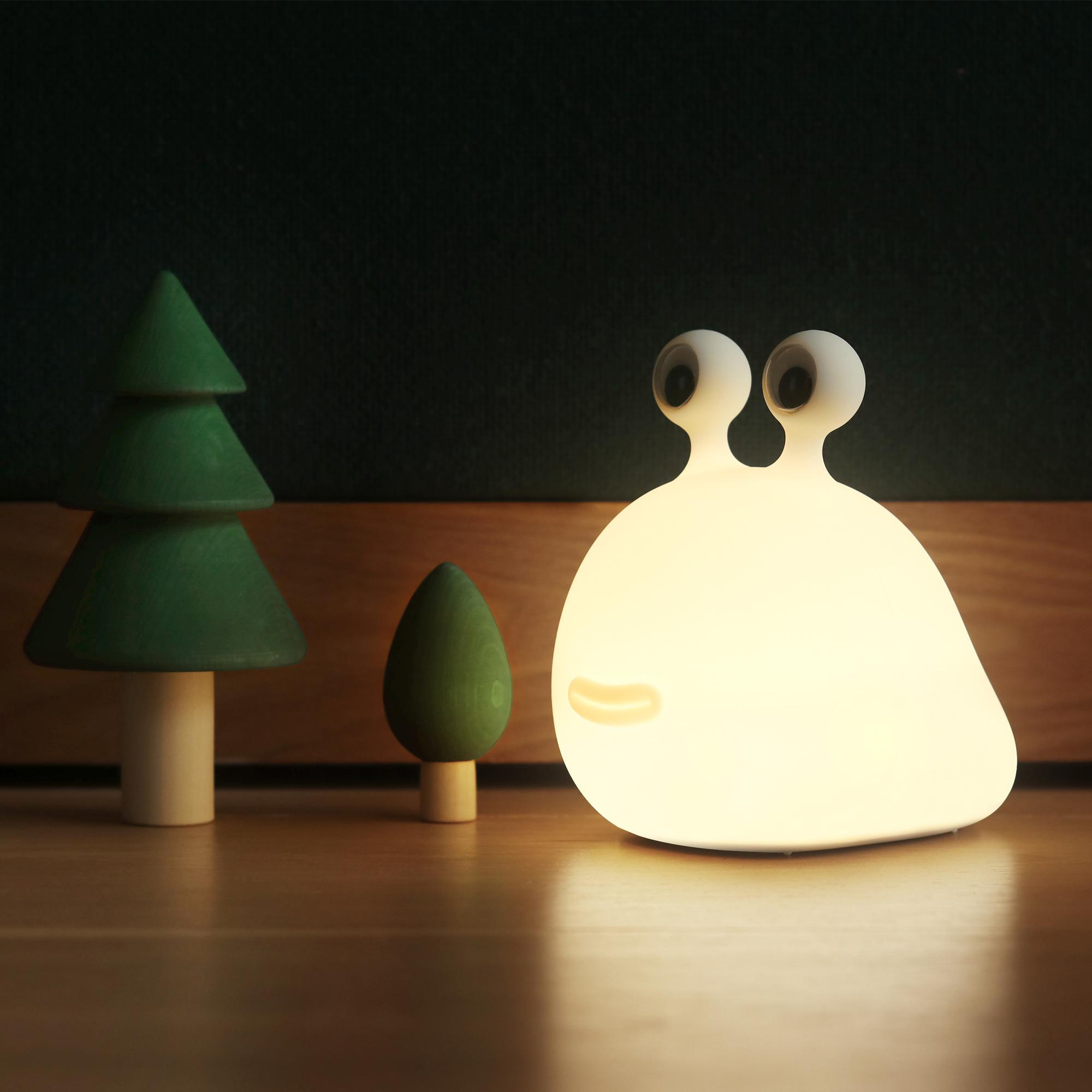 Leuchtende, weiße, schneckenförmige Lampe mit zwei Bäumen auf Holzoberfläche.