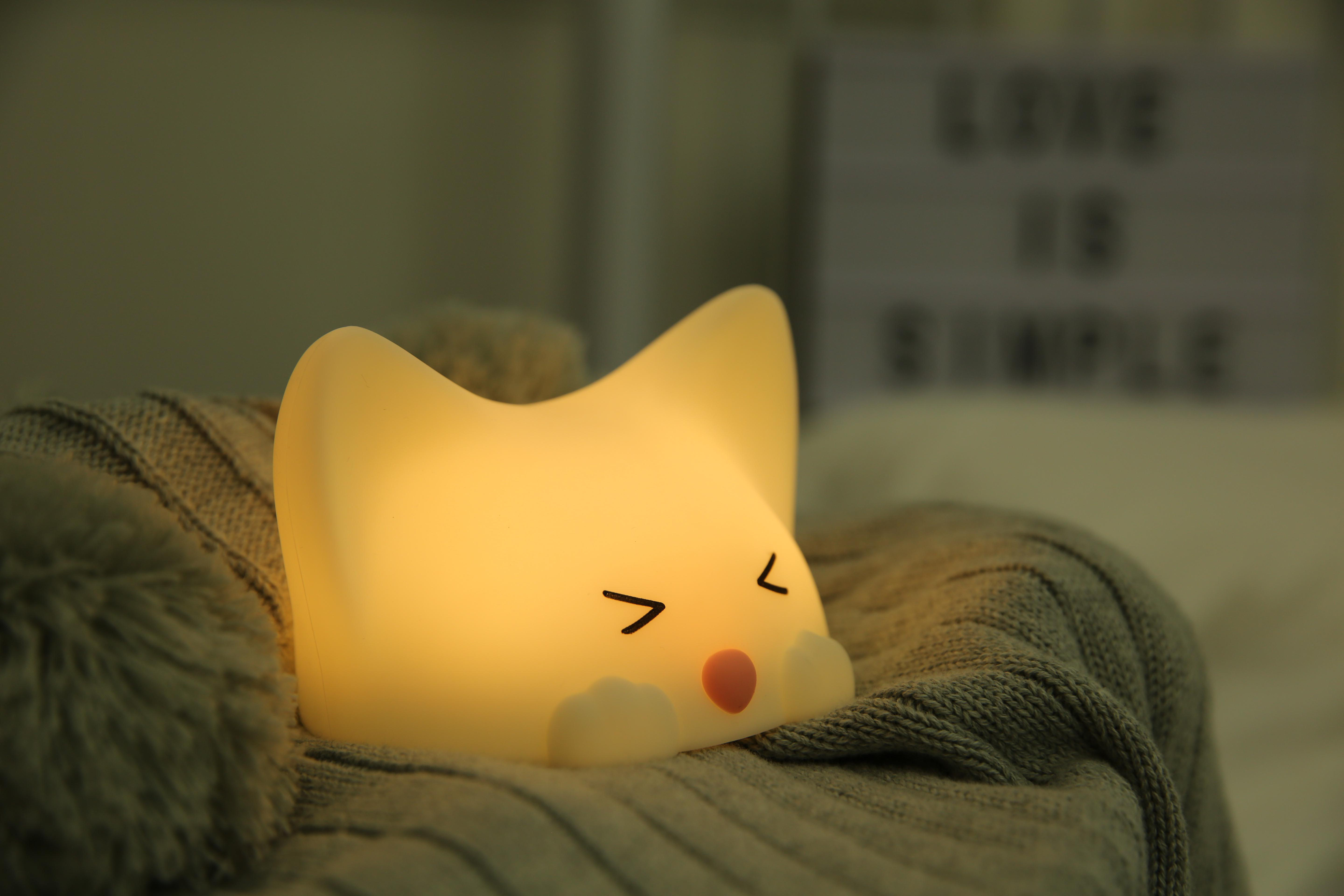 Ein leuchtendes, weißes, katzenförmiges Nachtlicht auf einer grauen Decke.
