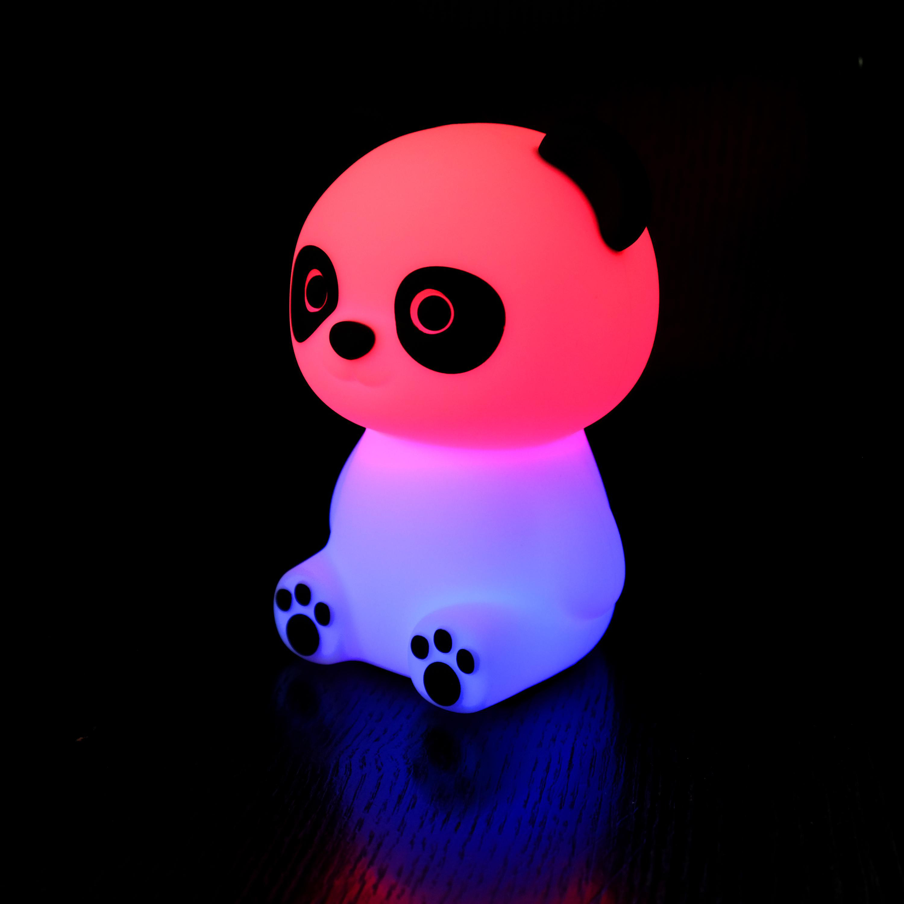 Ein leuchtendes Panda-Nachtlicht, rosa Kopf und weißer Körper, auf schwarzem Untergrund.