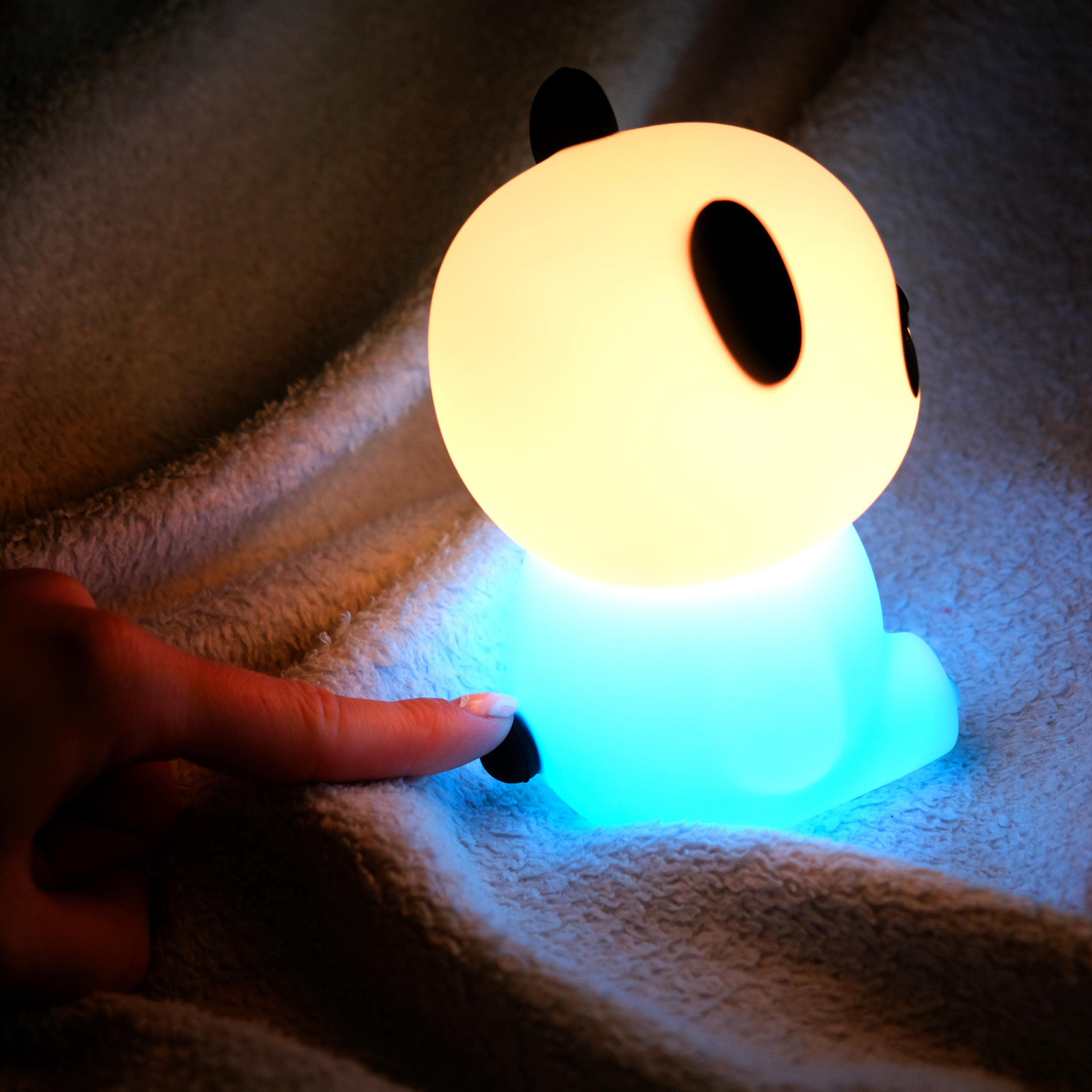 Panda-förmige Lampe. Sie leuchtet sanft und wird von einem Finger berührt.