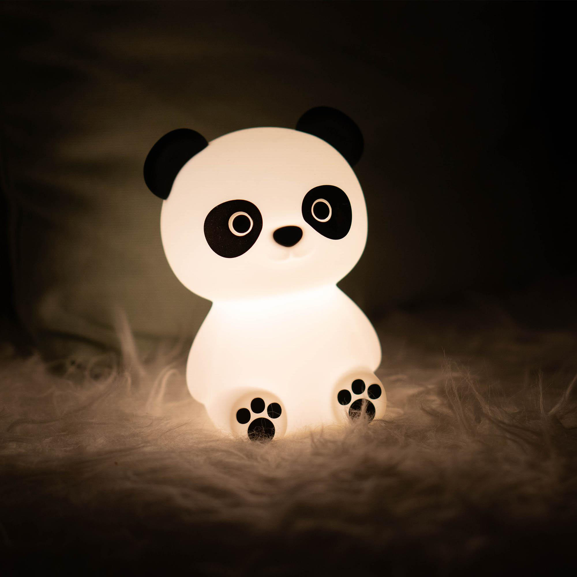 Ein leuchtendes panda-förmiges Nachtlicht auf einer flauschigen weißen Oberfläche in einem dunklen Raum.