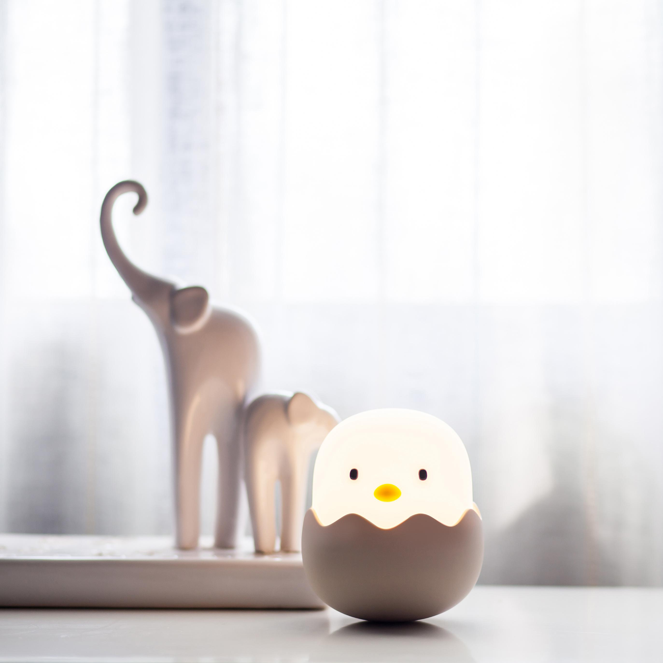 Eine leuchtende Küken-Lampe in einem Ei. Weiße Elefantenstatuen im Hintergrund.
