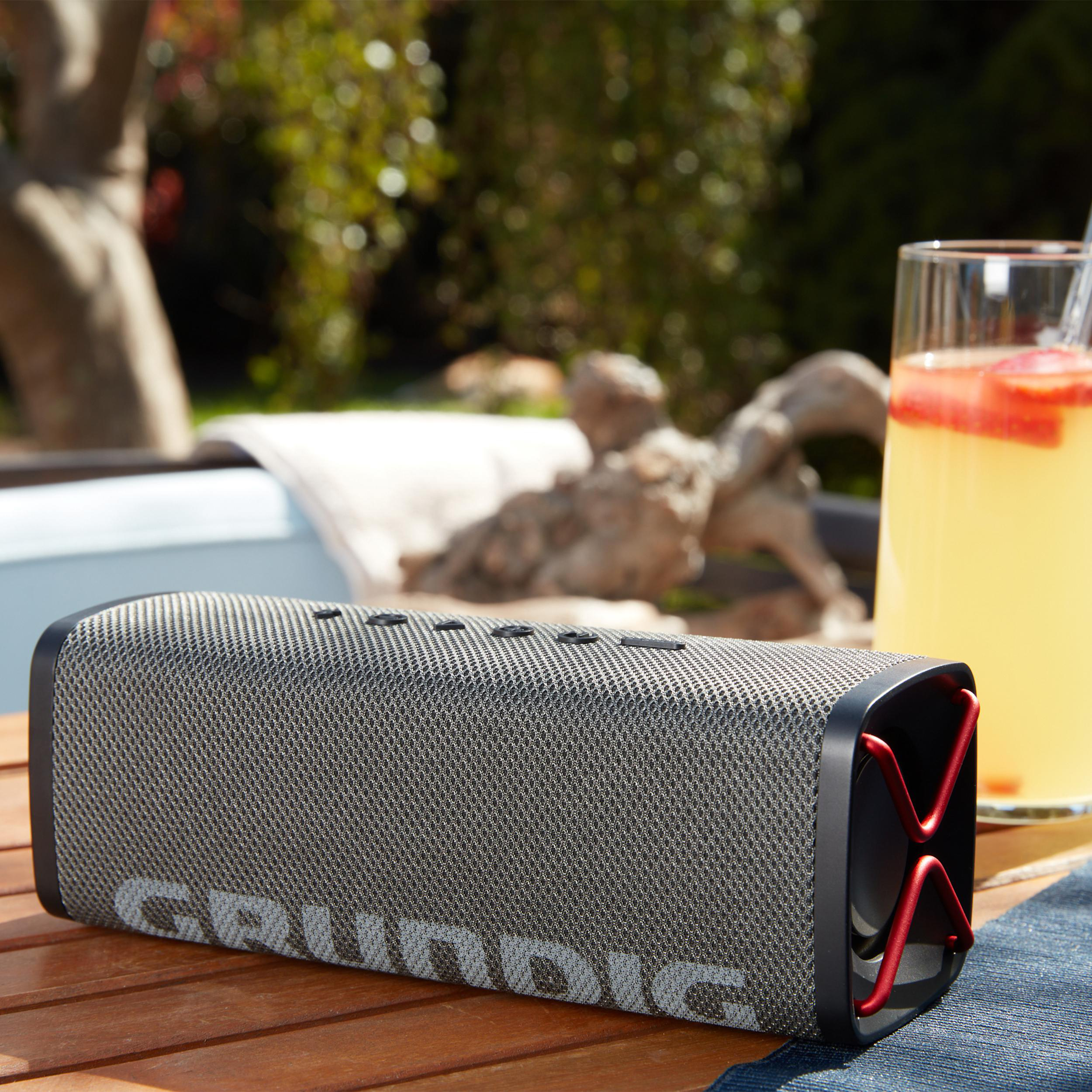 Ein grauer Grundig-Lautsprecher mit roten Akzenten steht auf einem Holztisch.