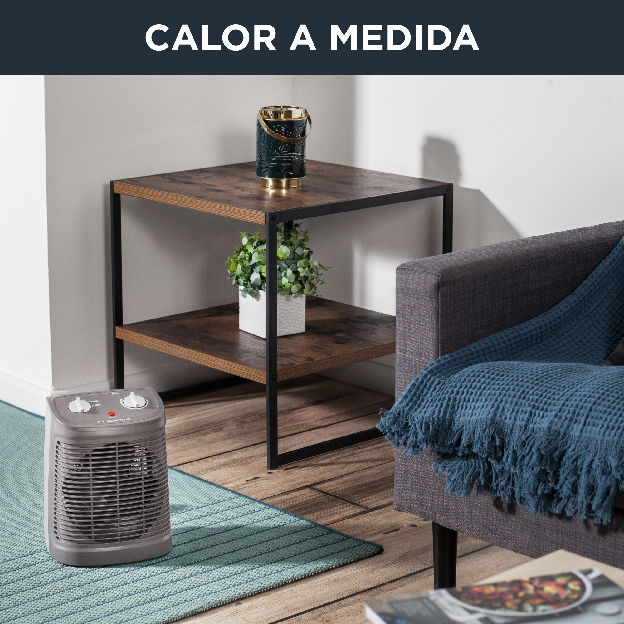 Un pequeño calefactor en una alfombra, cerca de una mesa de café y un sofá con una manta azul.