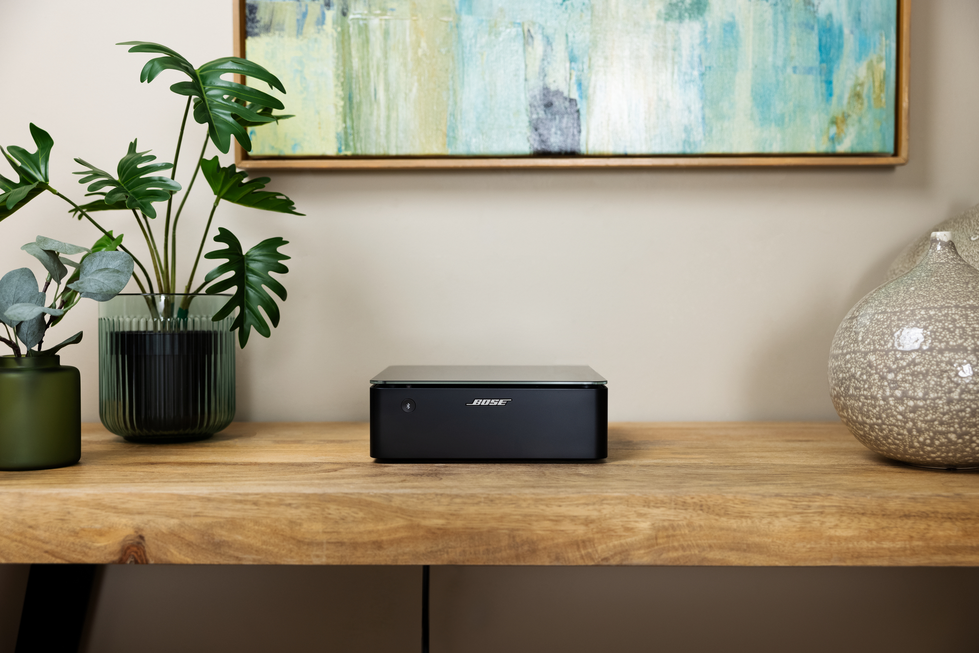 Ein schwarzes Bose-Soundsystem auf einem Holztisch, mit Pflanzen und Kunstwerken im Hintergrund.
