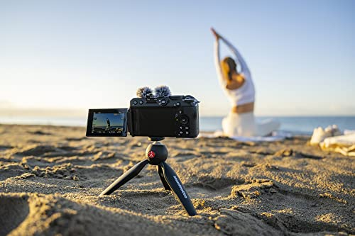 Una cámara en un trípode grabando a una mujer haciendo yoga en la playa al atardecer.