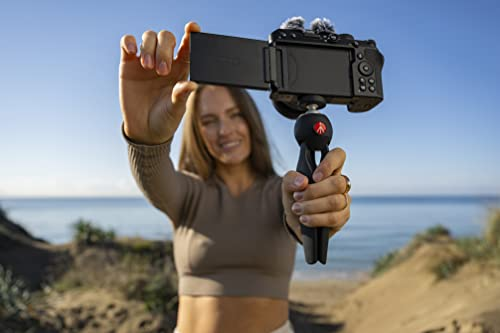 Mujer sosteniendo una cámara con micrófono. El fondo es una playa con cielo azul.