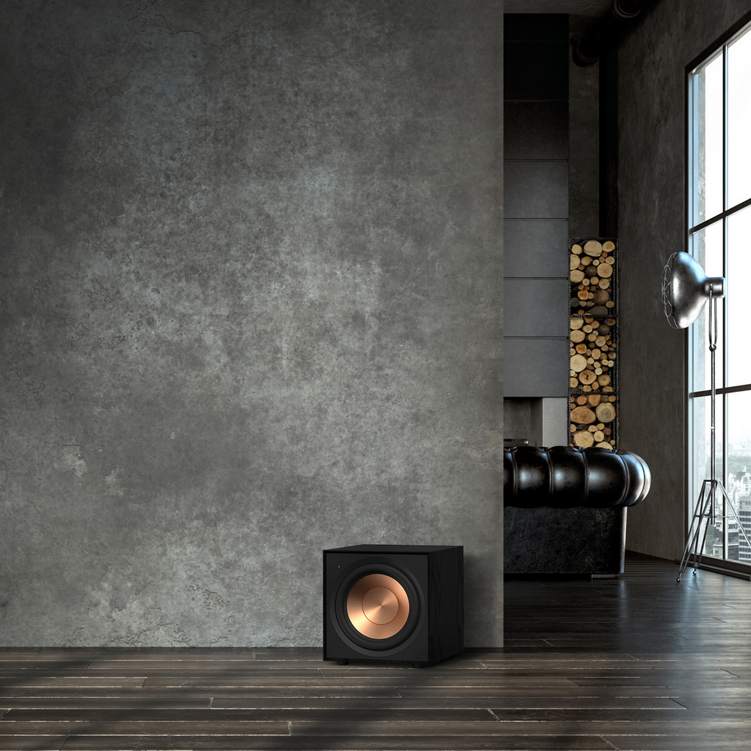 A black subwoofer speaker with a gold cone. It is in front of a concrete wall.