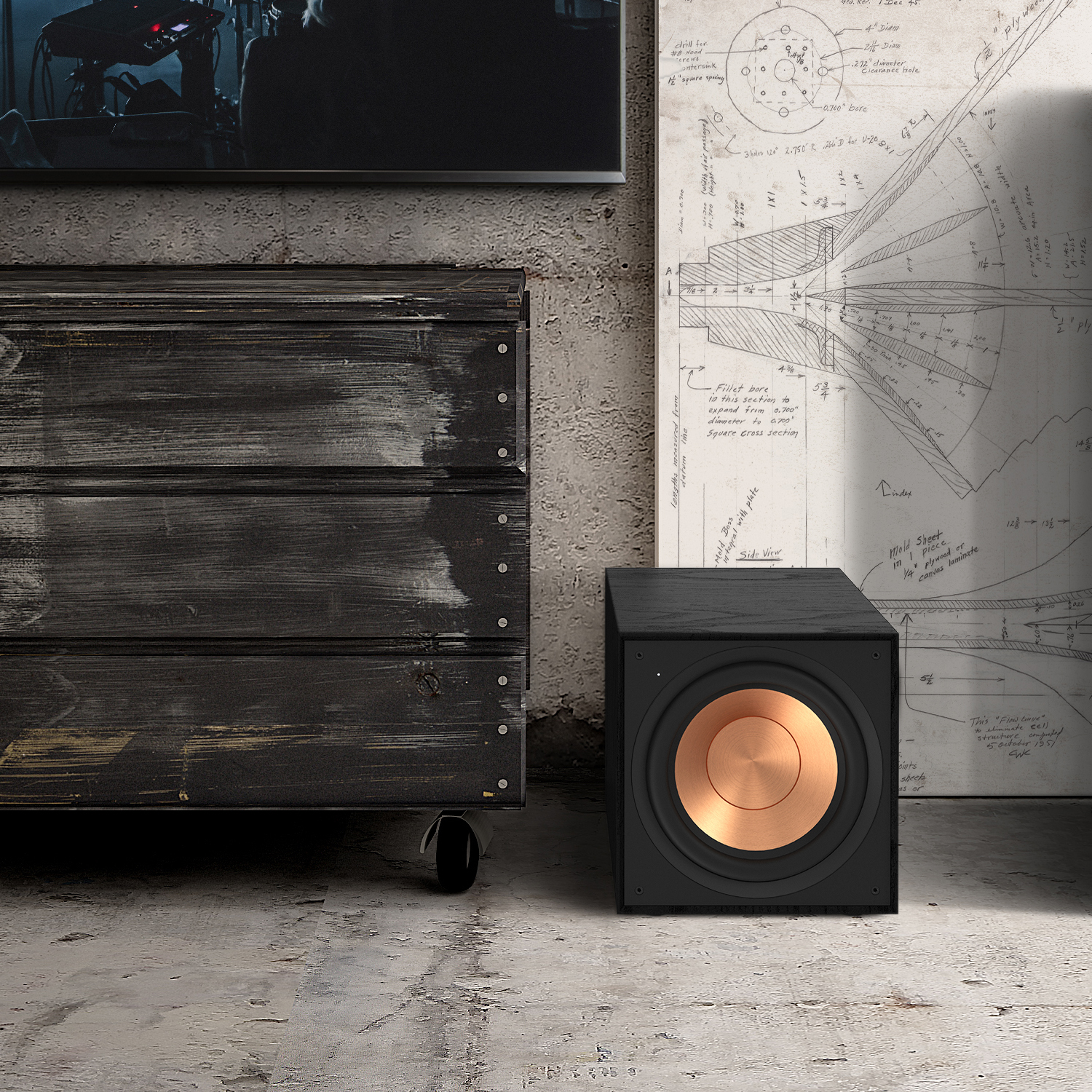 Black subwoofer with copper cone on the floor. A dark cabinet is on the left. A blueprint is in the background.