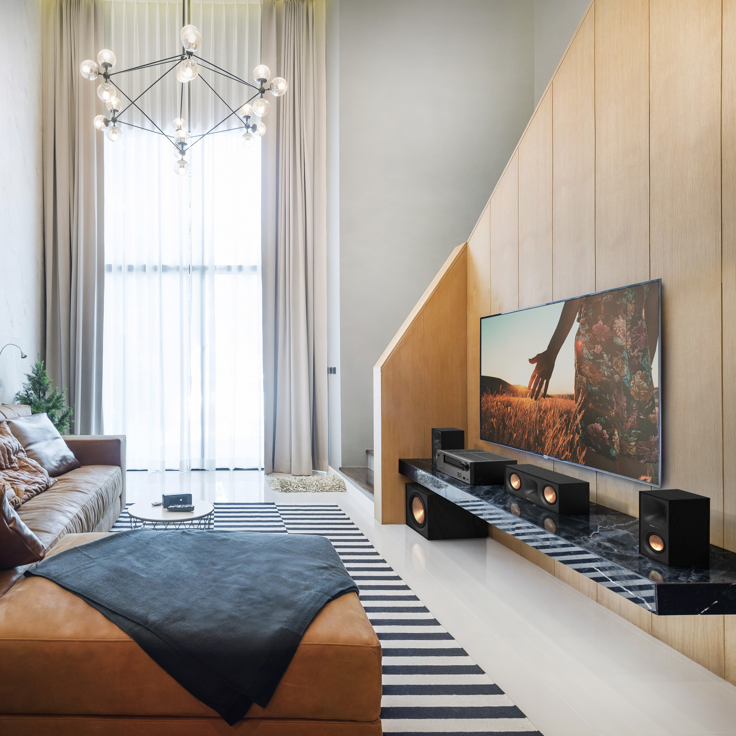 A modern living room with a brown leather couch, TV, and speakers, with a large window.
